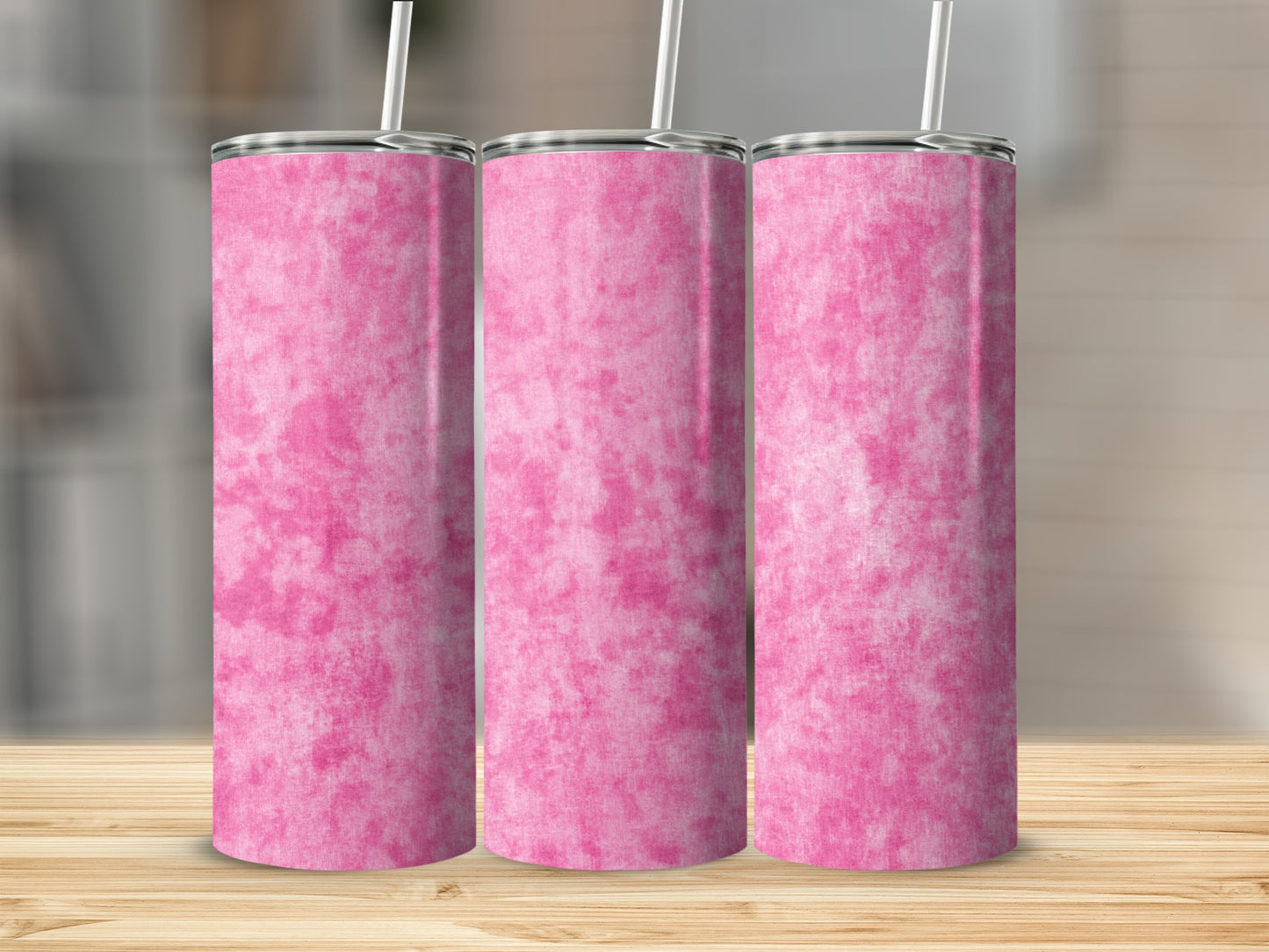 Three pink tie-dye patterned tumblers with straws on a wooden surface.