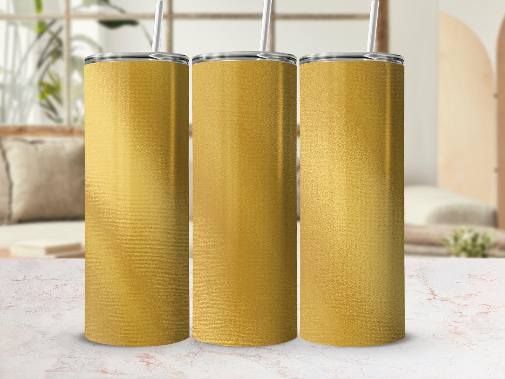 Three gold tumblers with silver lids and straws are displayed on a marble surface.