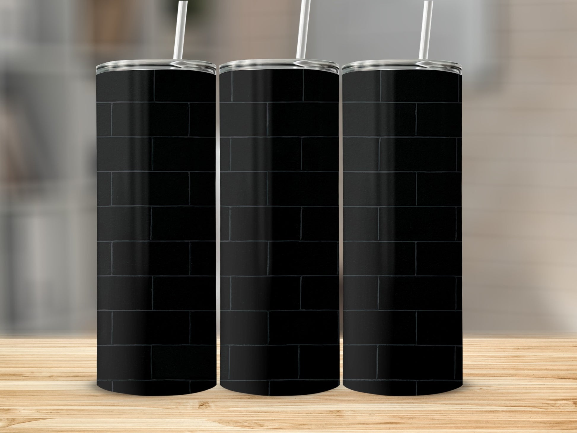 Three black brick pattern tumblers with white straws on a wooden surface.