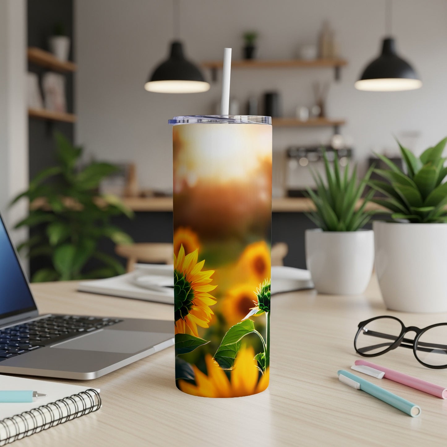 Sunflower tumbler with straw on desk with laptop and pens.