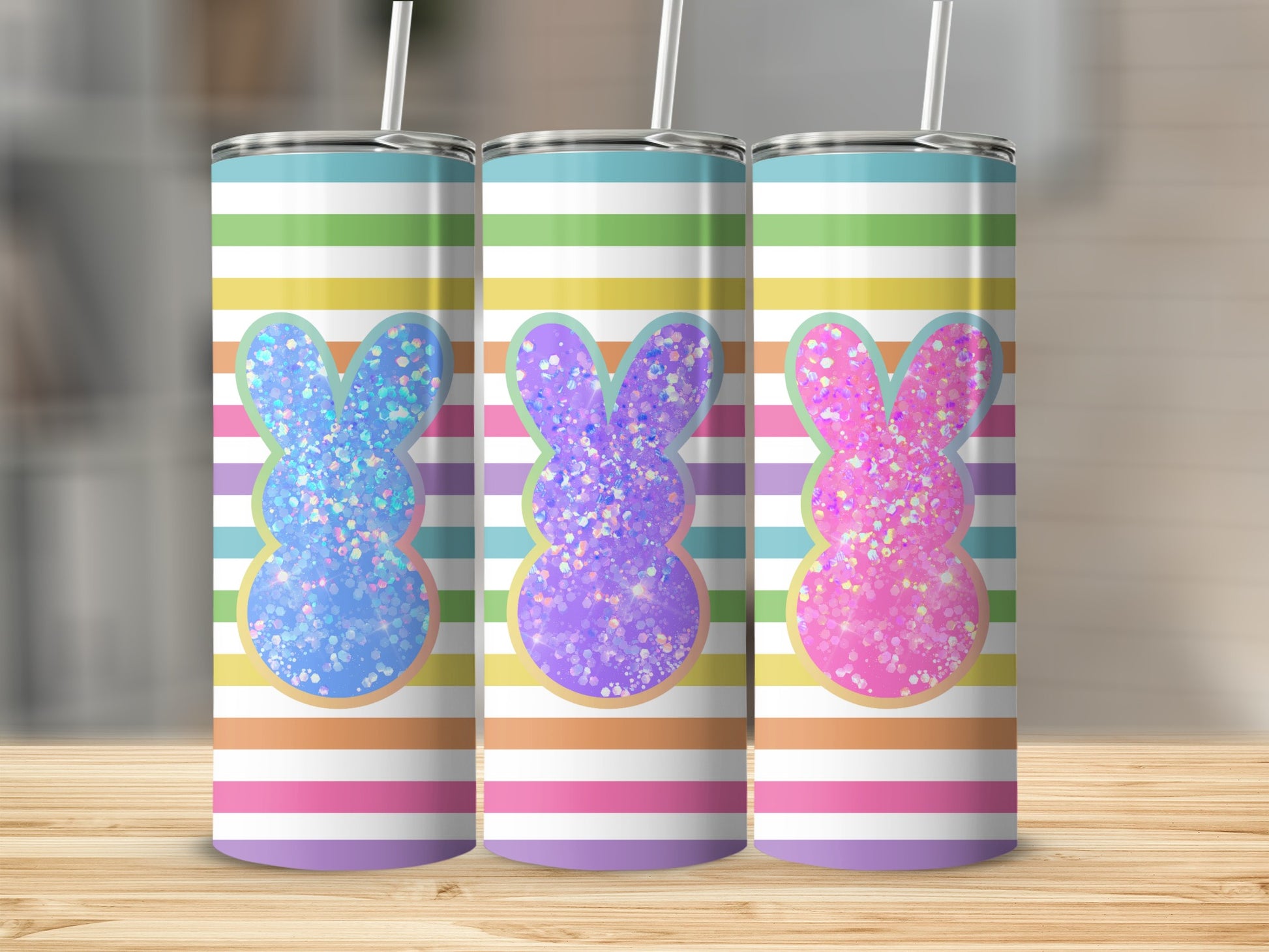 Three glitter bunny tumblers with striped backgrounds on a wooden surface.