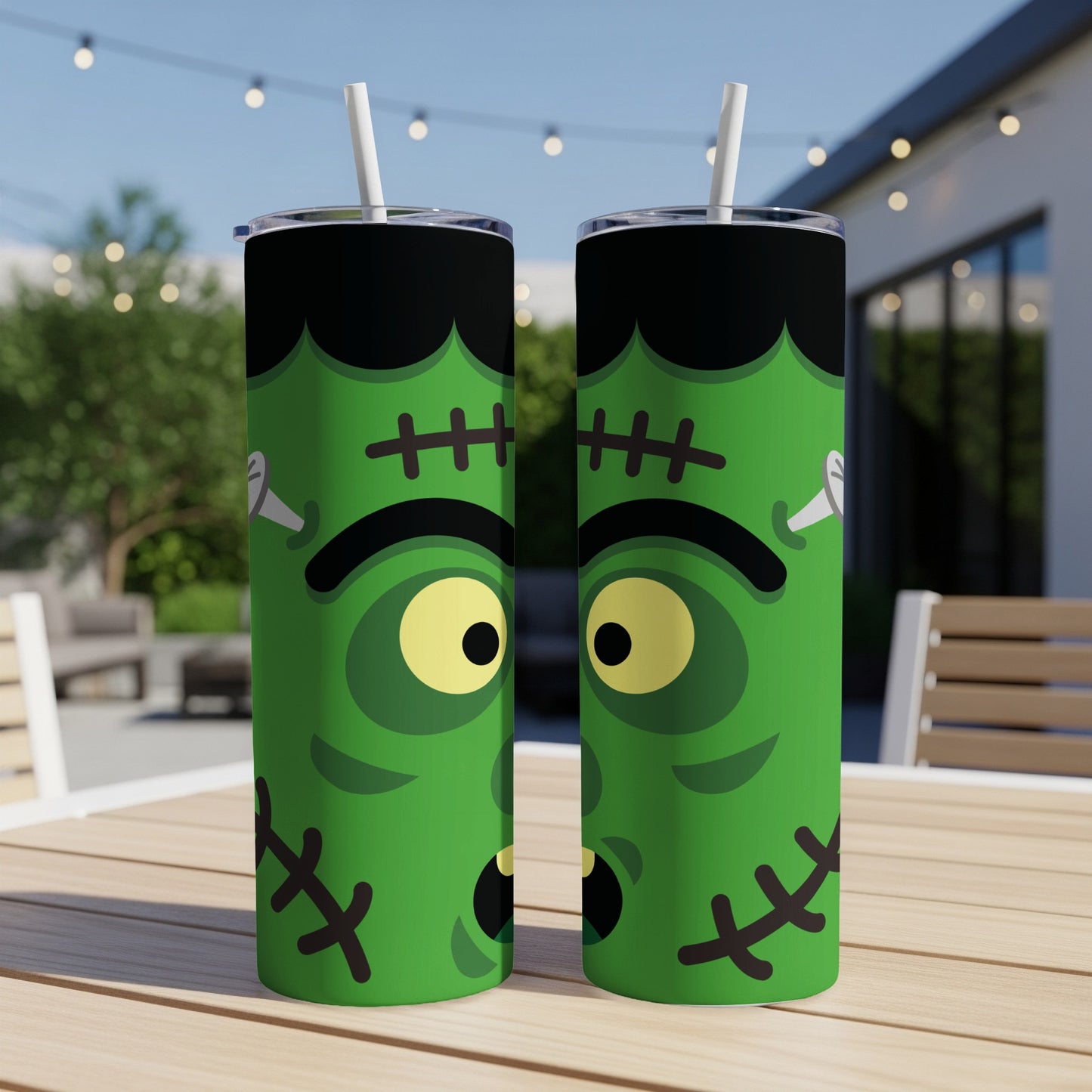 Two green tumblers with Frankenstein monster faces and straws on a table.