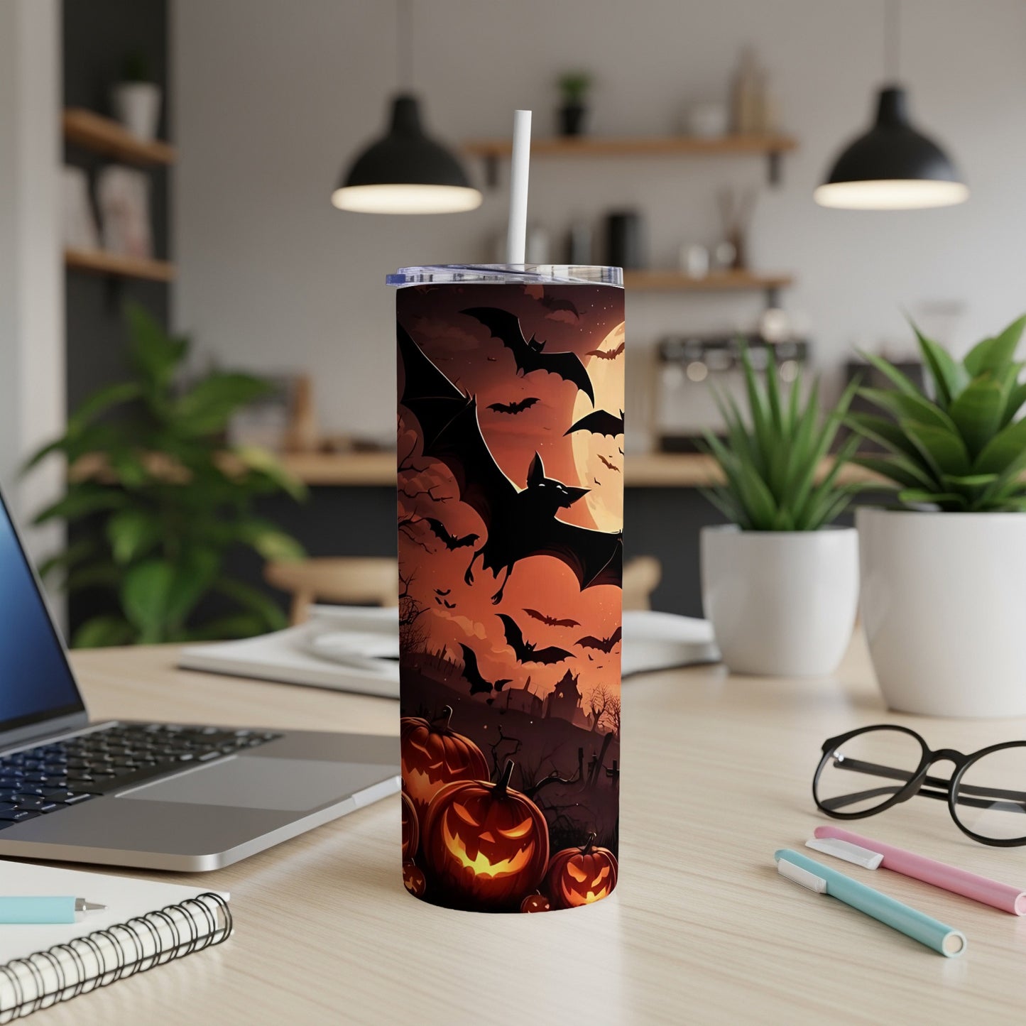 Halloween tumbler with bats, pumpkins, and a full moon on a desk.