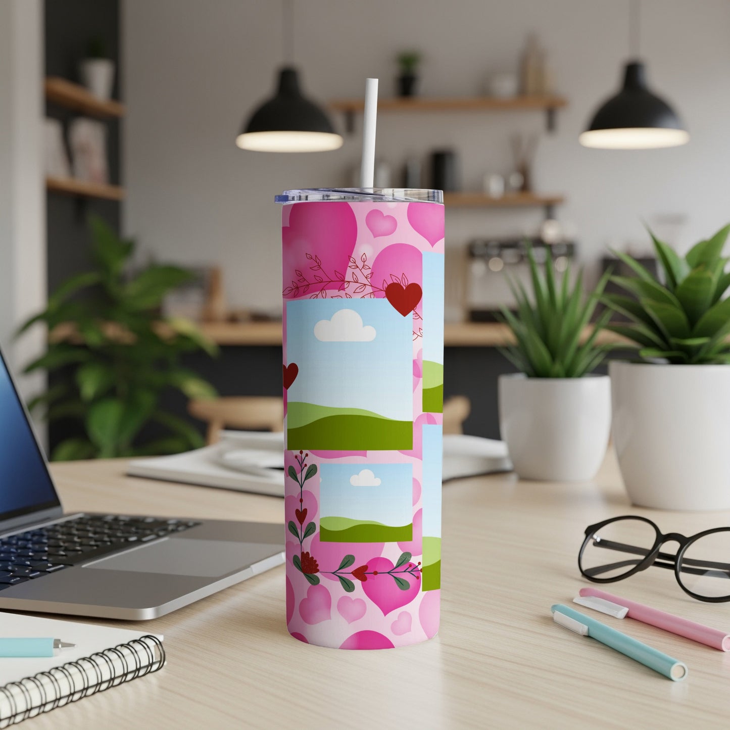 Pink tumbler with hearts and landscape photo frames, on a desk.