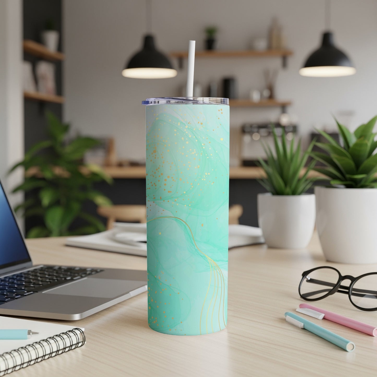 Mint green tumbler with gold swirls and straw on a desk.