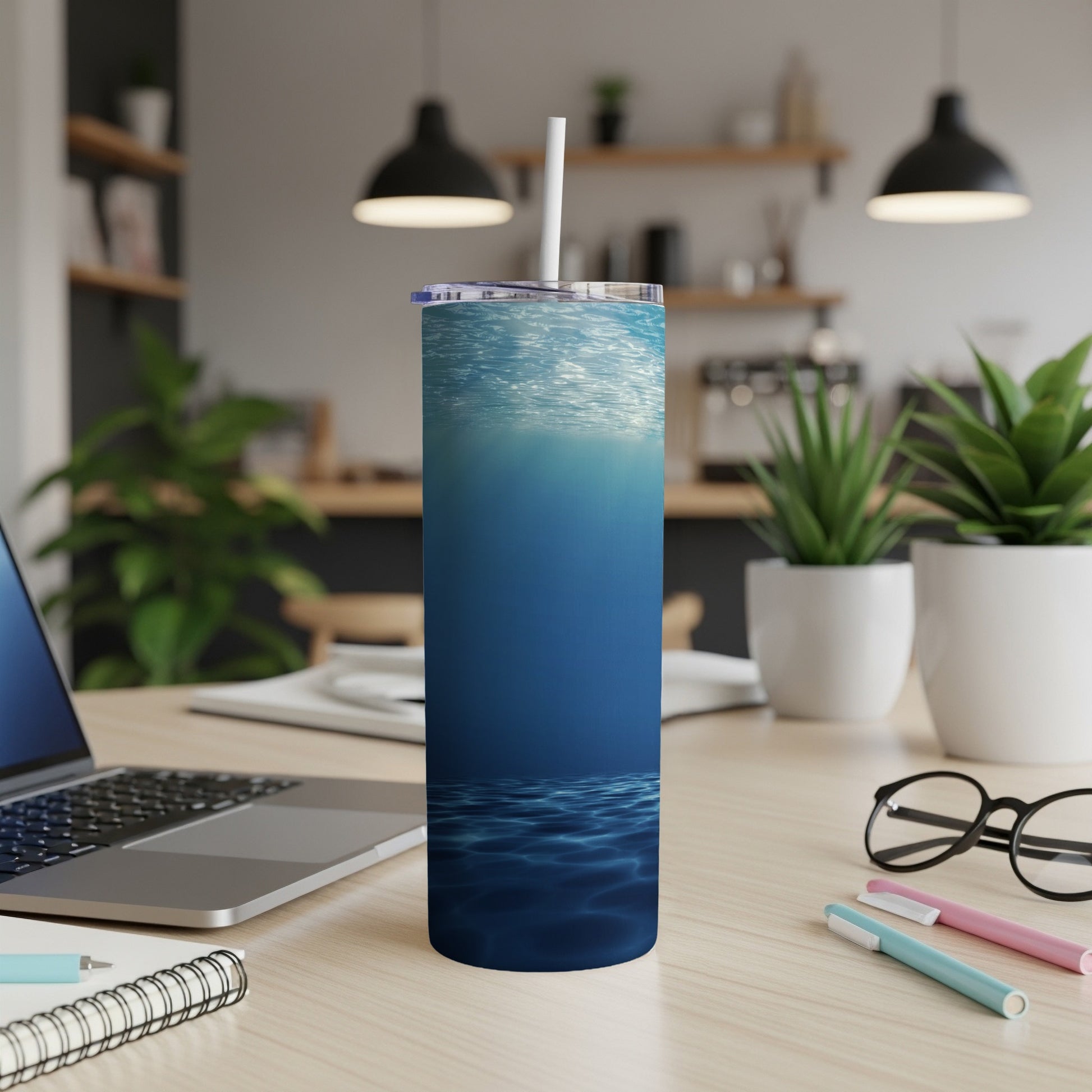 Blue tumbler with underwater ripple design, straw and lid, on desk.