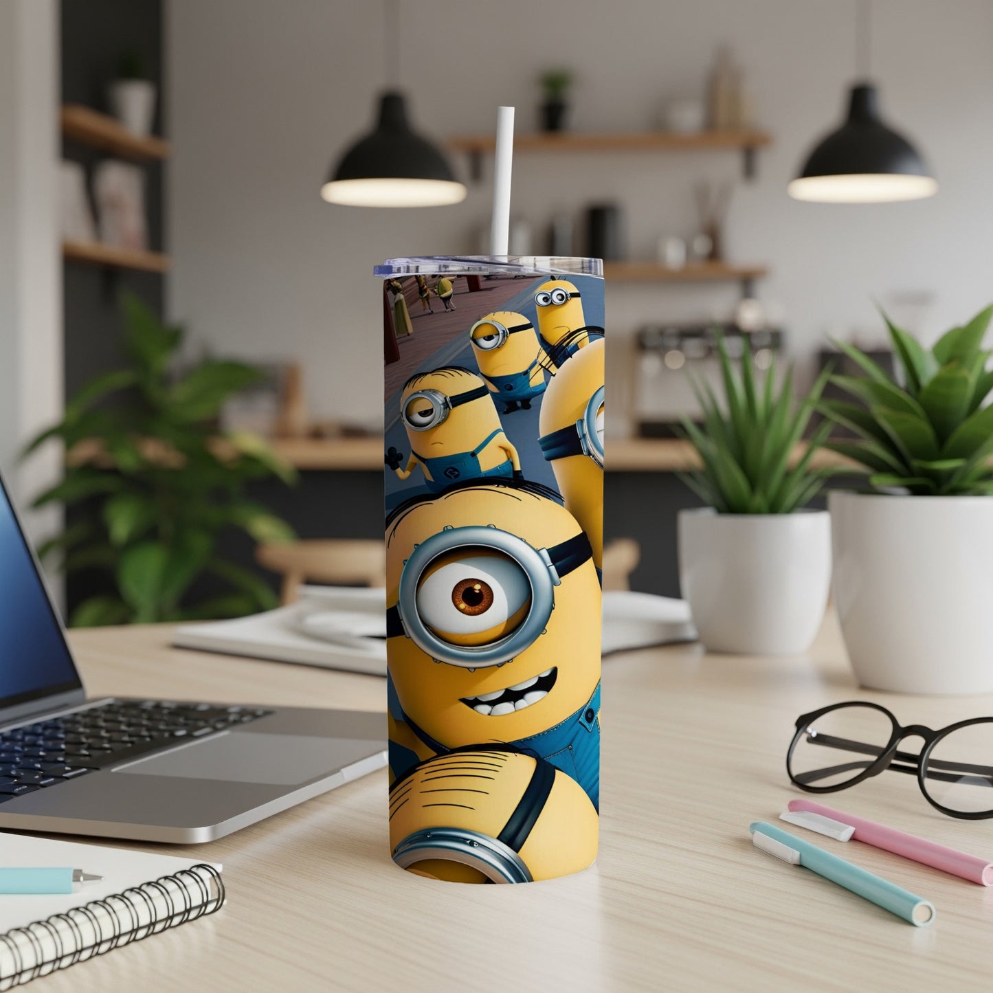 Minions on a tall yellow tumbler with a straw and laptop in background.