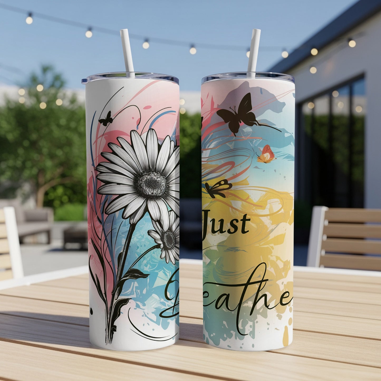 Two tumblers with floral and butterfly designs on a wooden table outdoors.