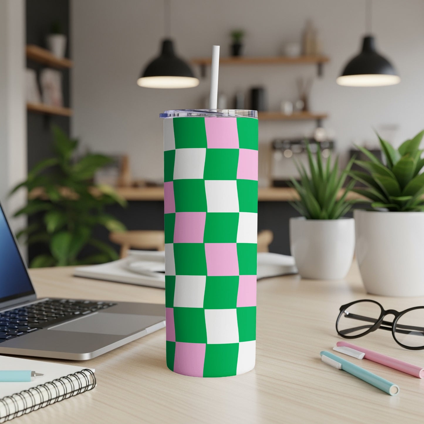 Green and pink checkered tumbler with straw on desk.