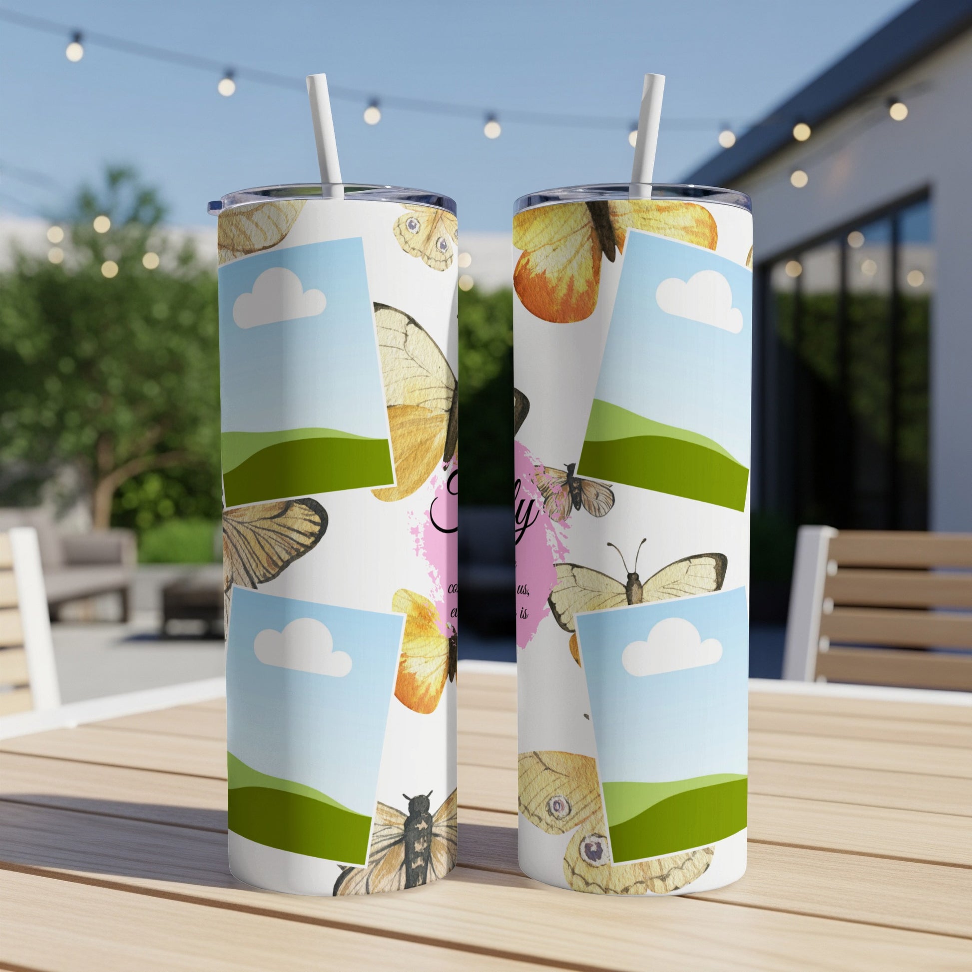Two tumblers with butterfly and cloud designs displayed on a wooden table outdoors.