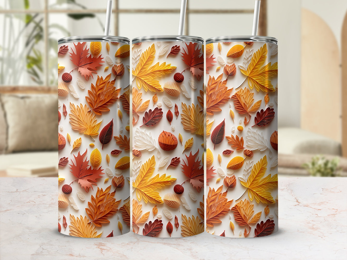 Three tumblers with a fall leaf pattern, white straws, on a marbled surface.