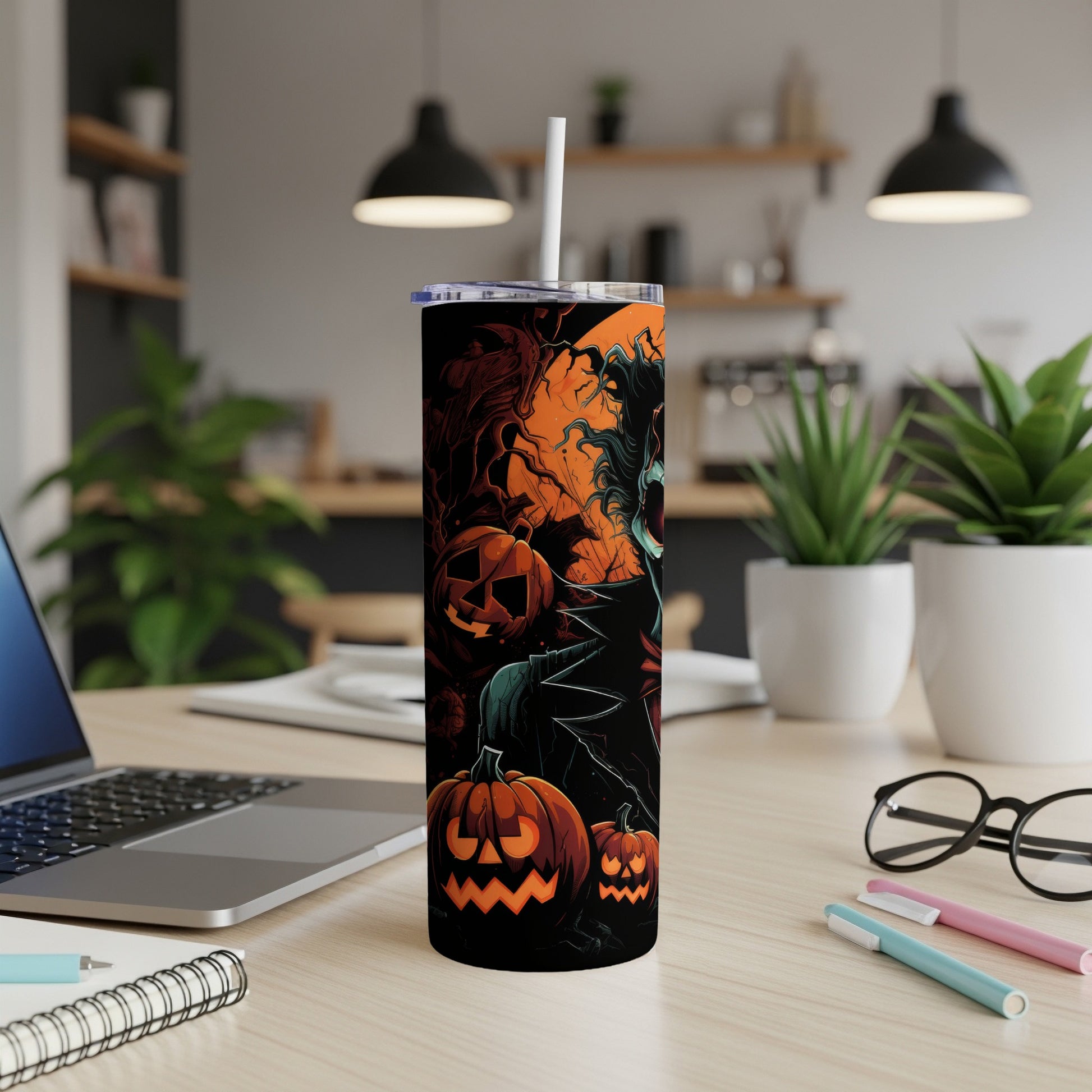 Halloween tumbler with jack-o'-lanterns and spooky figures on a desk.