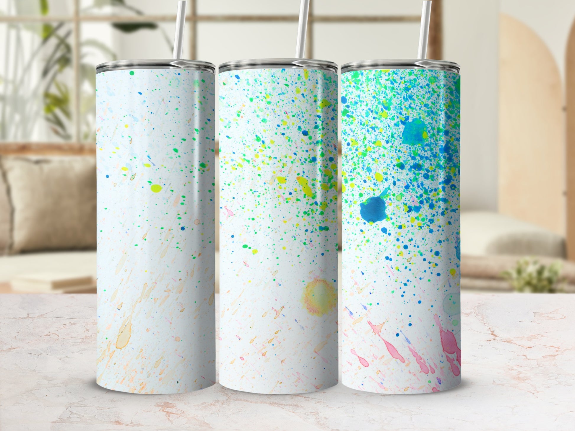 Three tumblers with colorful paint splatter design on white background.