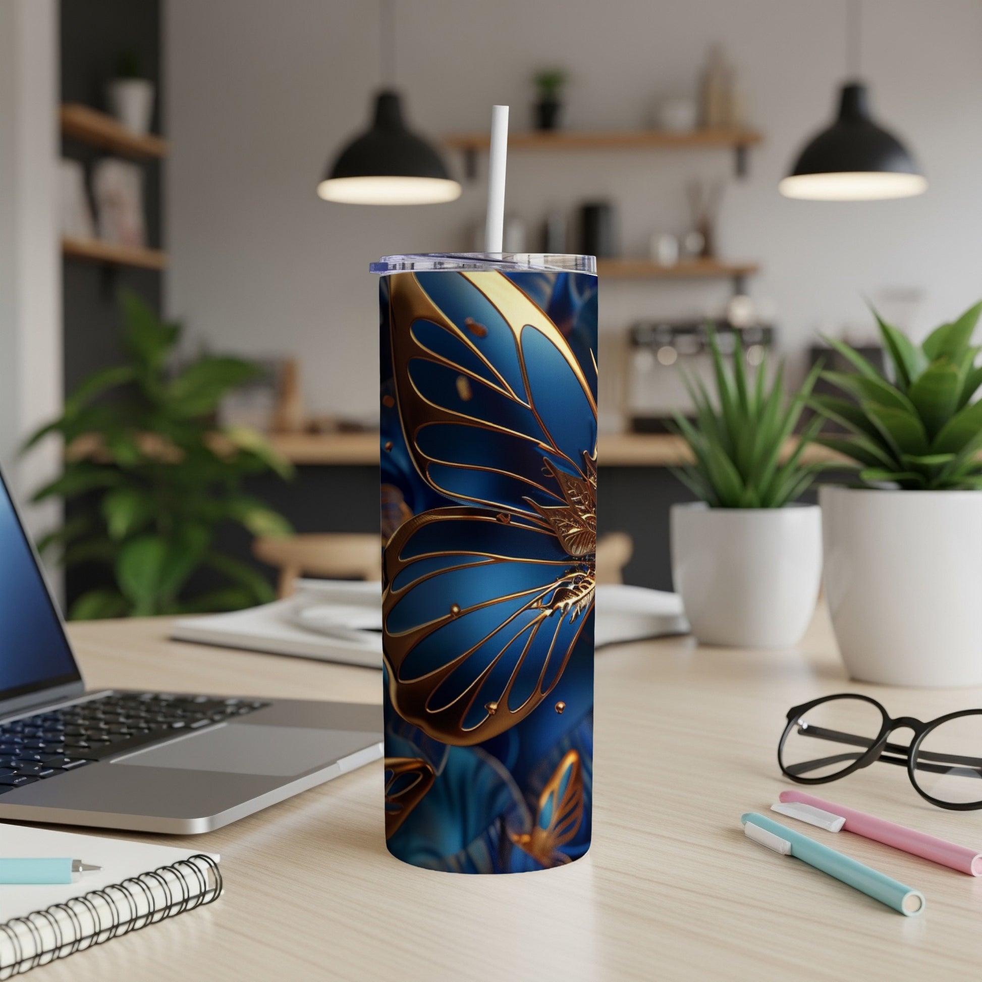 Gold butterfly design on a blue tumbler with a straw, on a desk.
