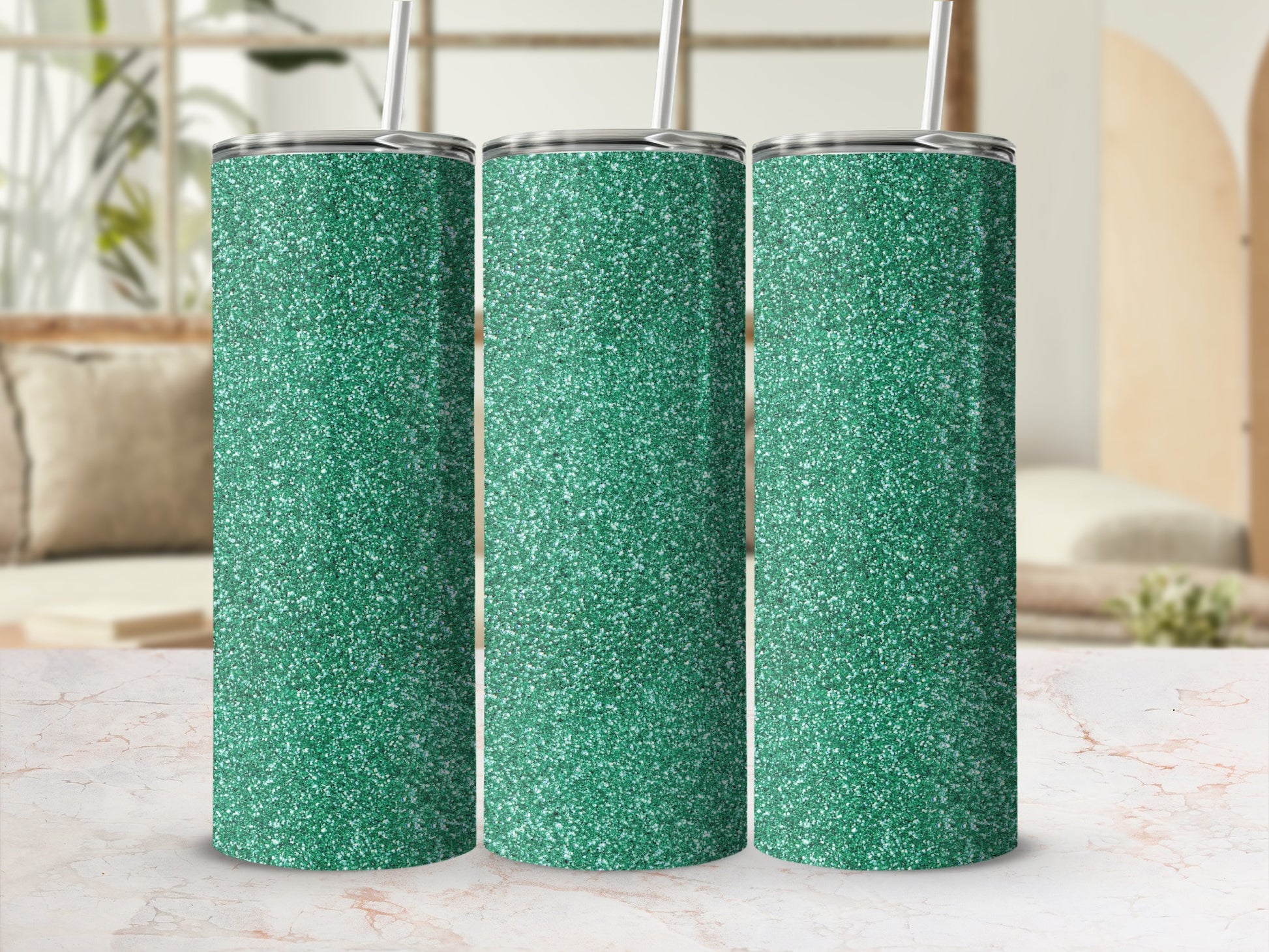 Three green glitter tumblers with silver lids and straws on a marble surface.