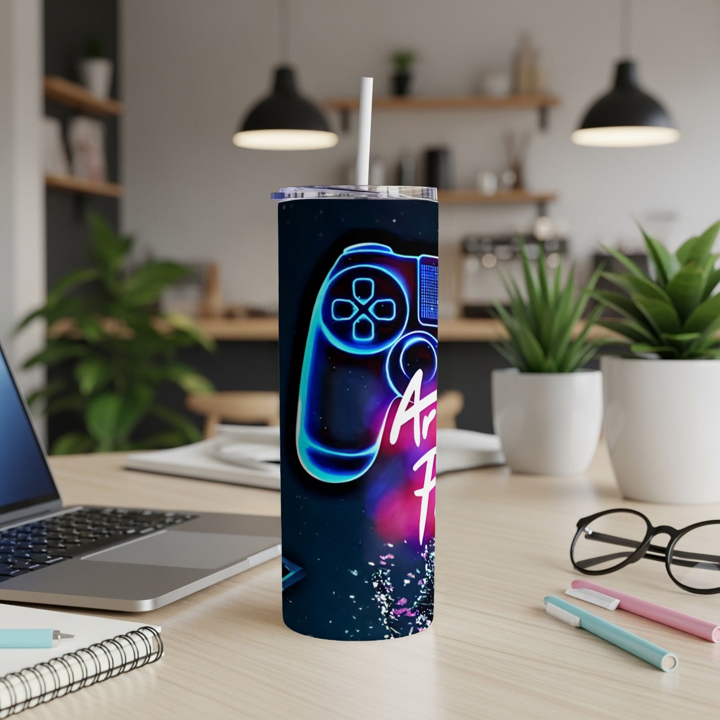 Neon game controller design on a tall tumbler with a straw, on a desk.