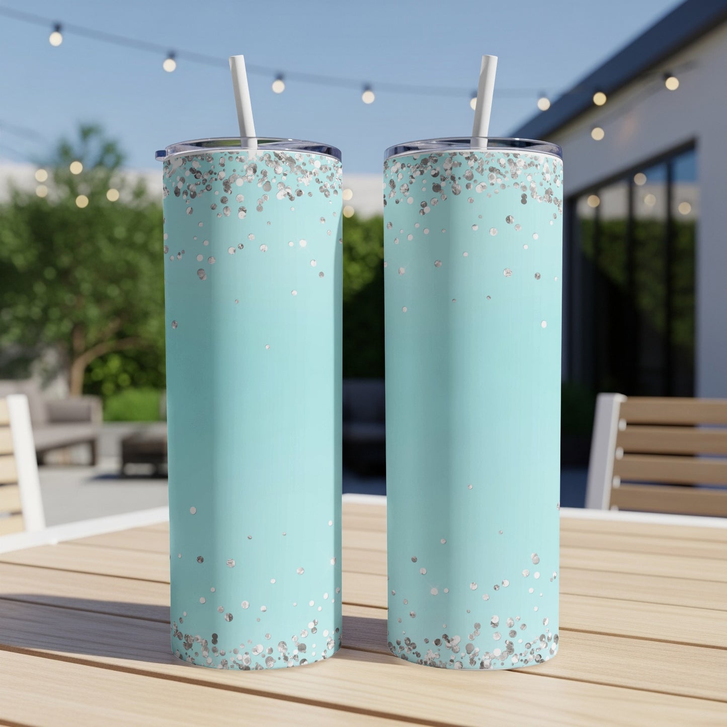 Two aqua tumblers with silver confetti pattern and straws on a wooden table.