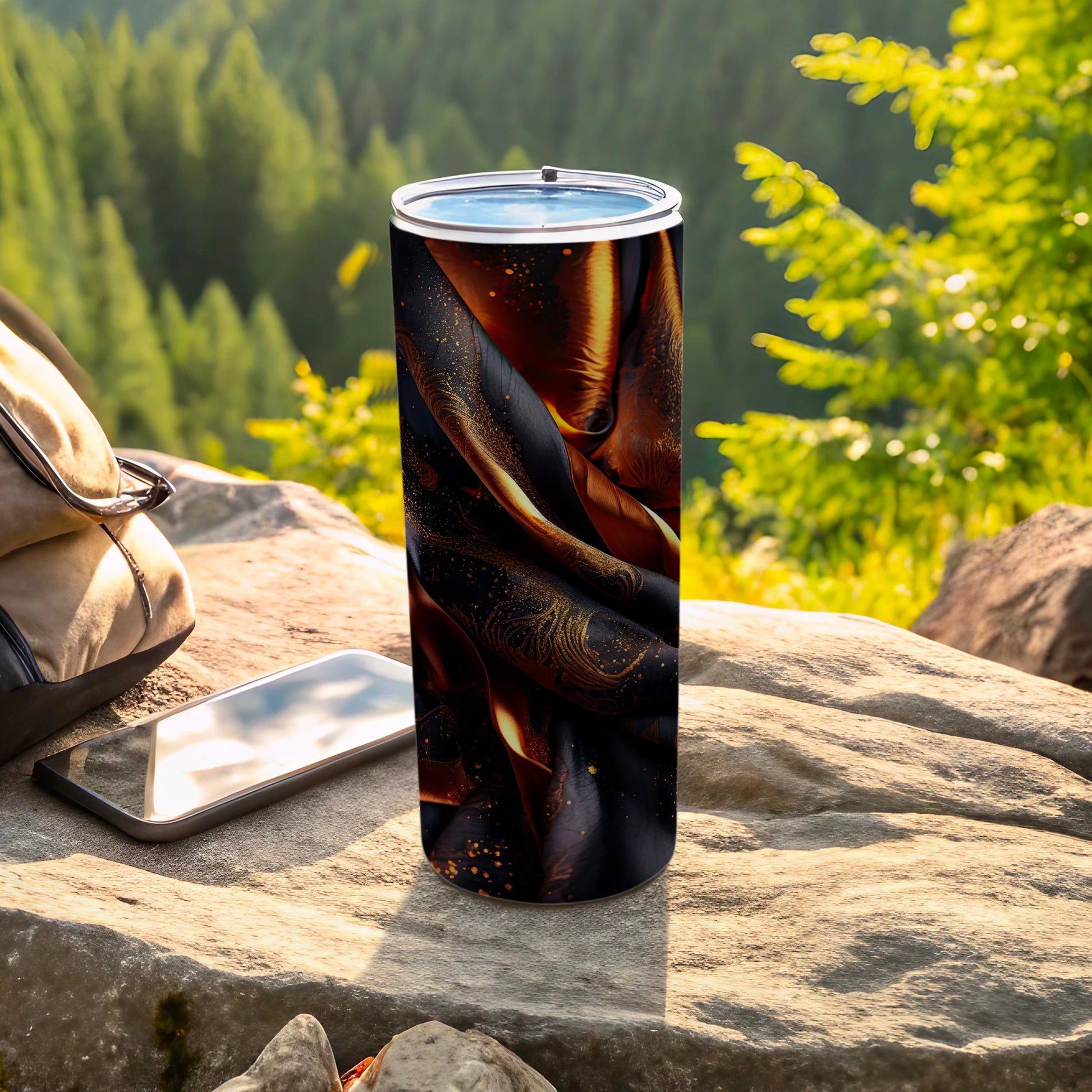 Black and gold abstract pattern tumbler on a rock with a phone.