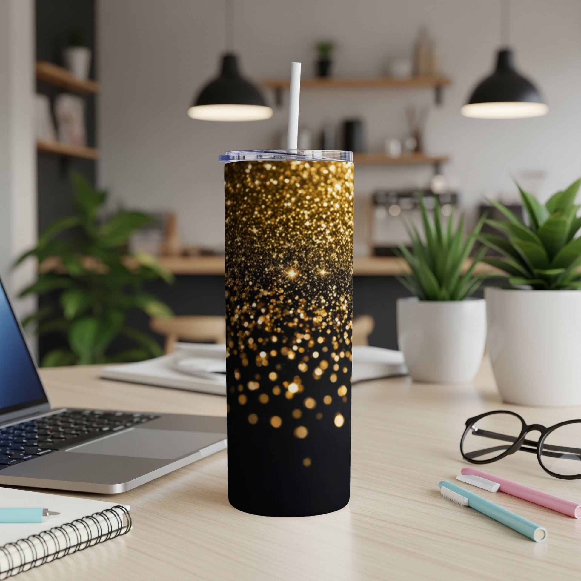 Black tumbler with gold glitter design and white straw on a desk.