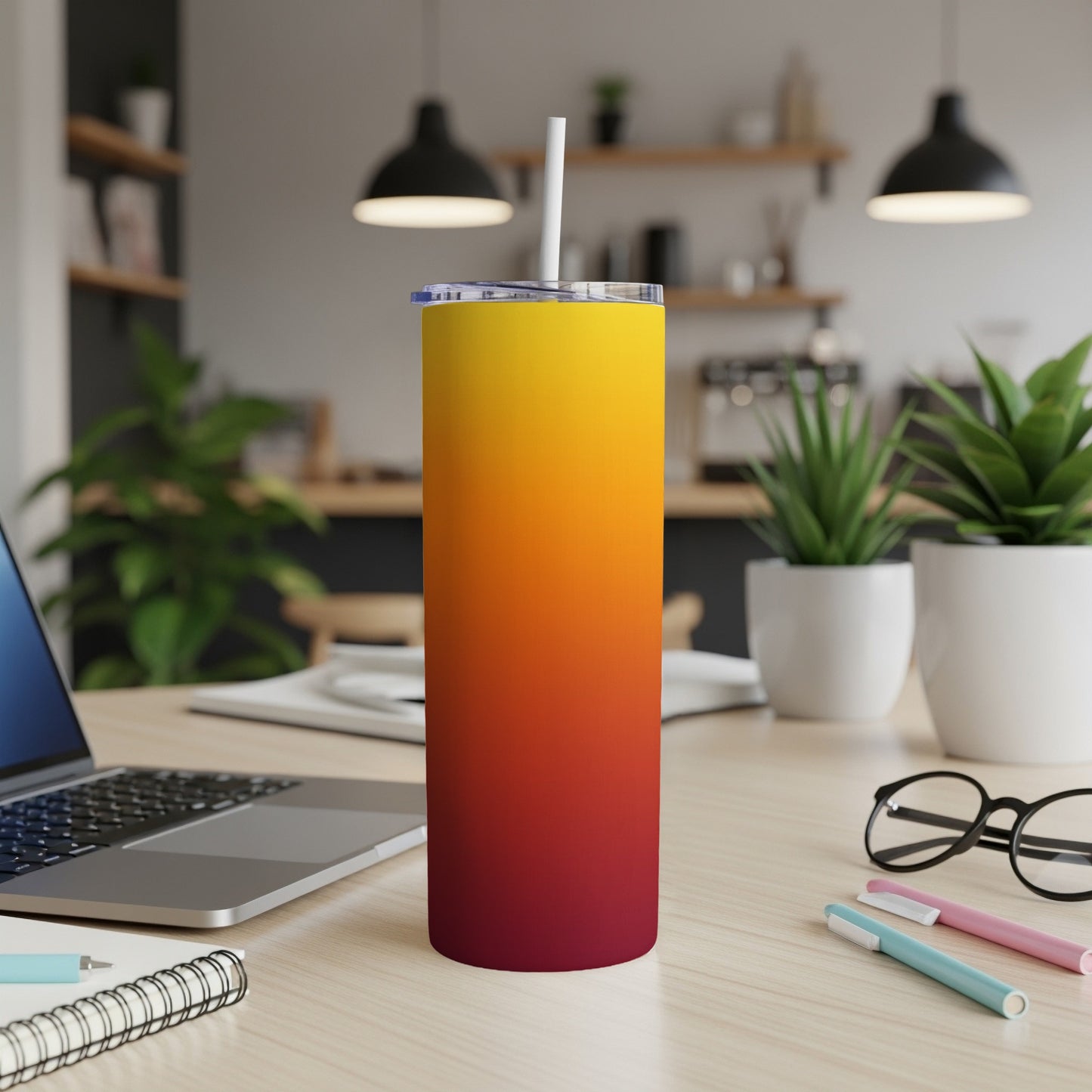 Gradient sunset tumbler with straw on a desk next to a laptop.
