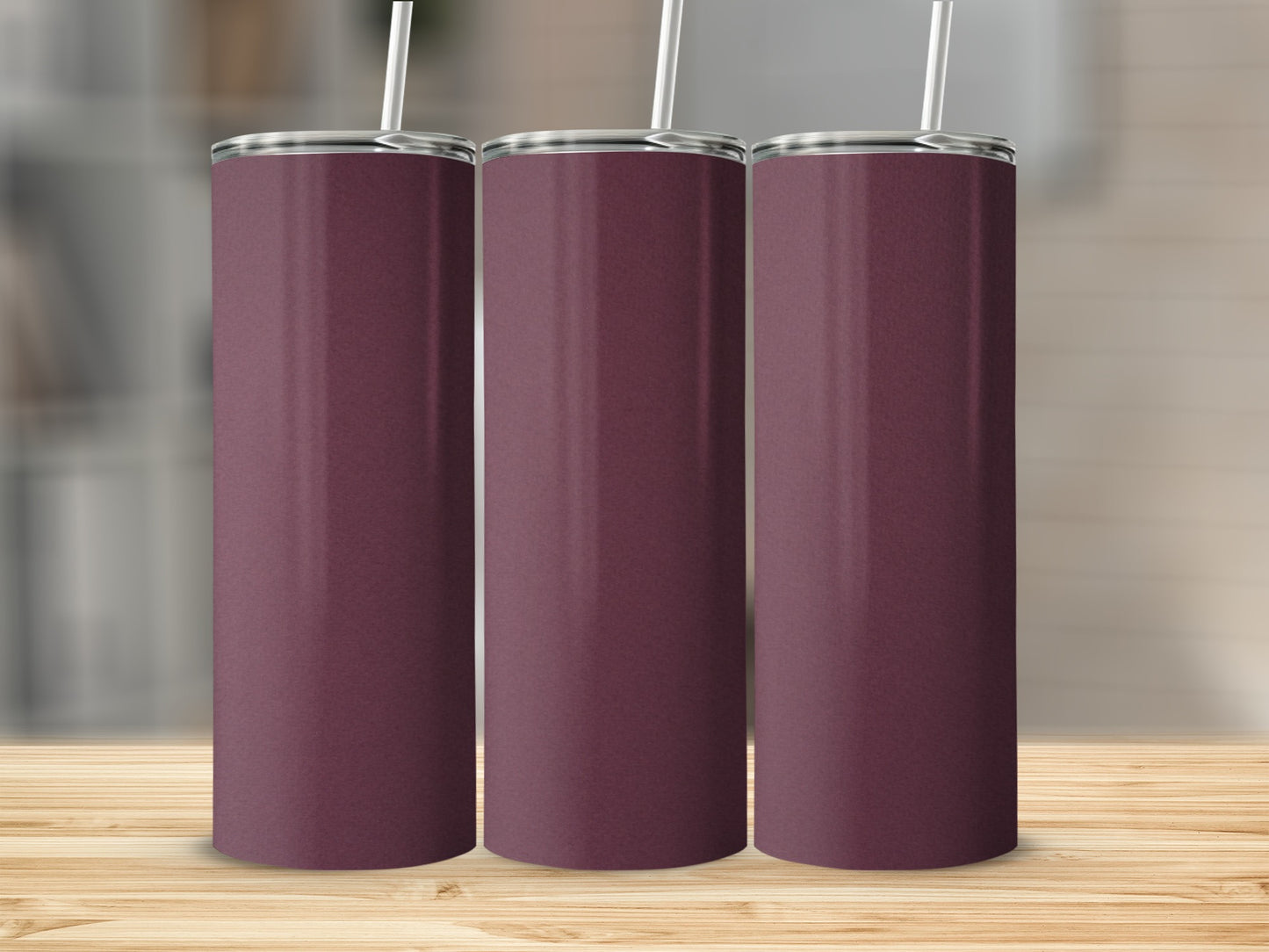 Three plain burgundy tumblers with straws stand on a wooden surface.