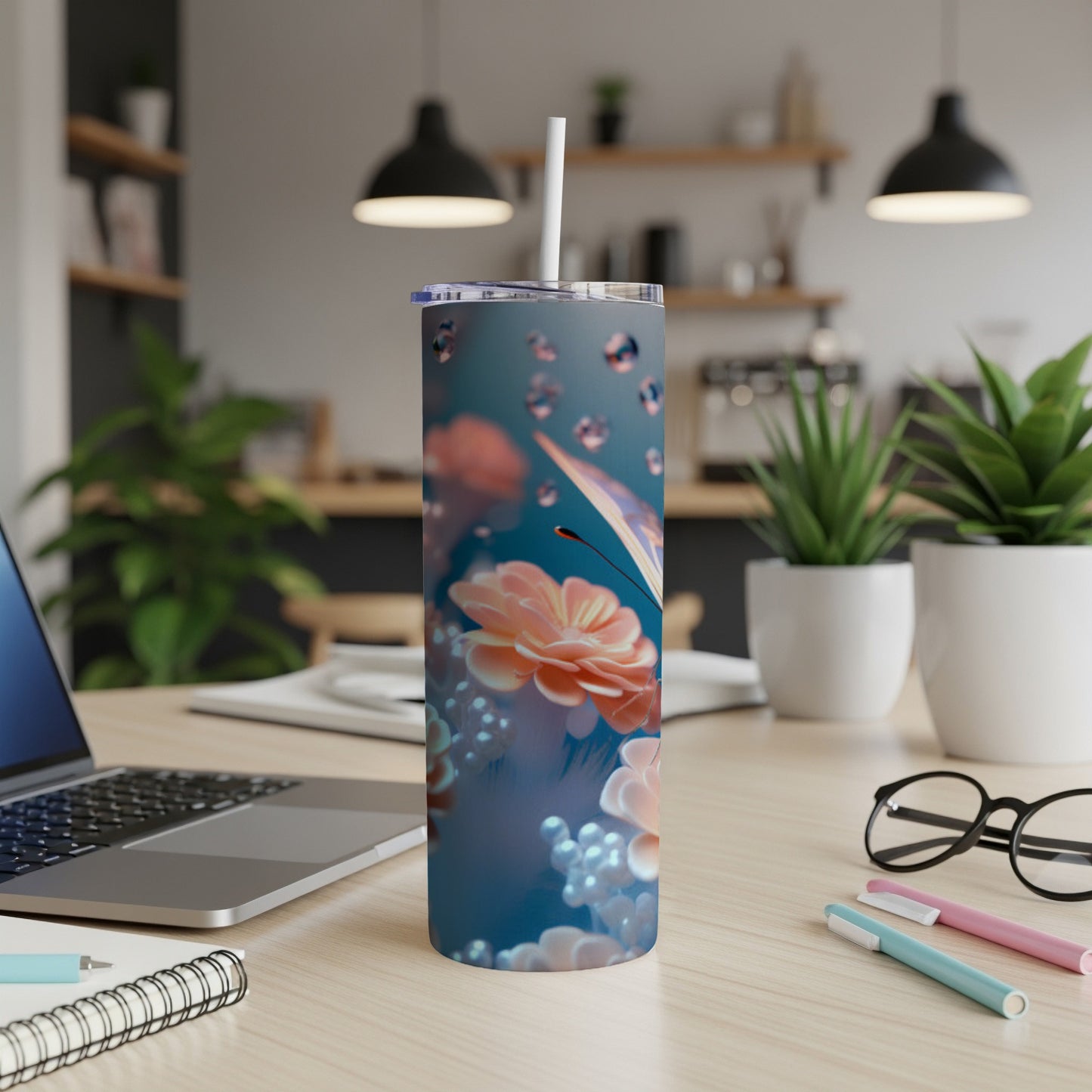 Floral butterfly tumbler with straw on a desk with plants and pens.