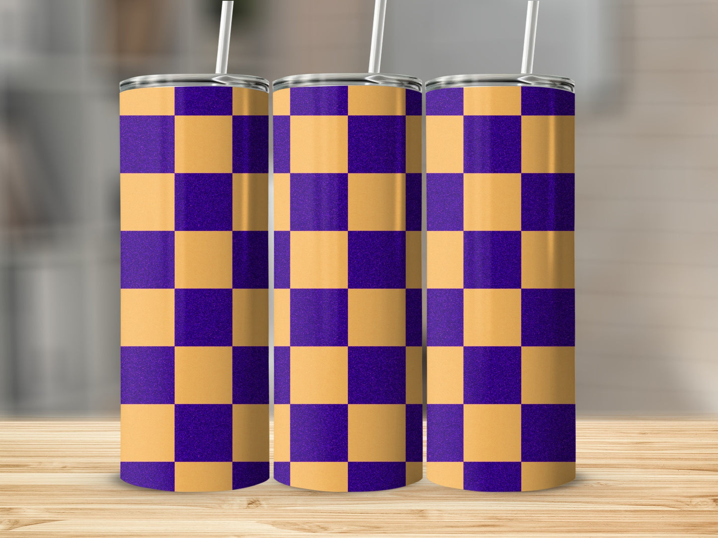 Three purple and gold checkerboard pattern tumblers with straws on a wooden surface.