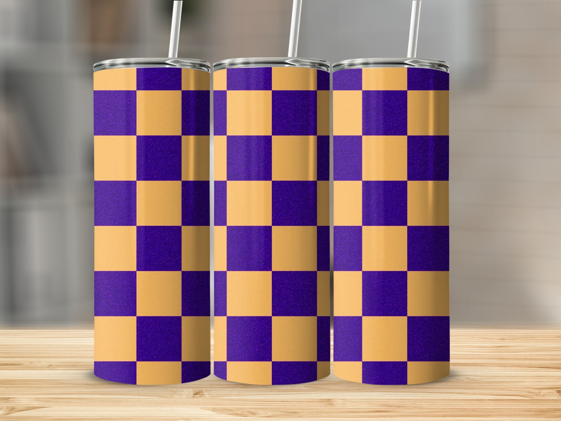 Three purple and gold checkerboard pattern tumblers with straws on a wooden surface.