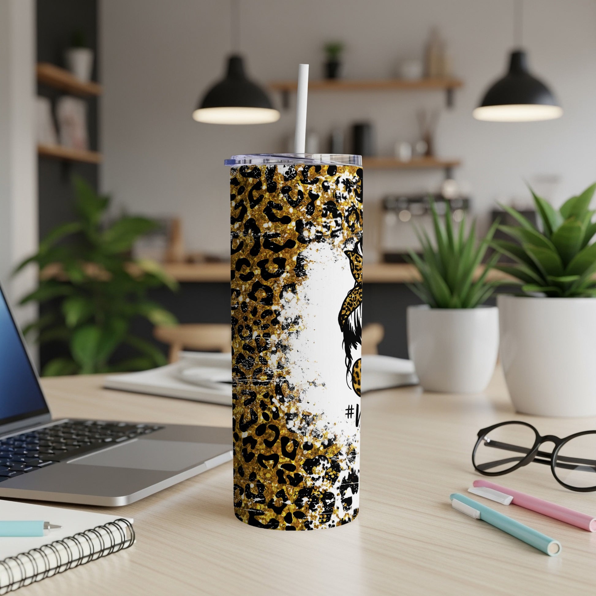 Leopard print tumbler with white straw on desk next to laptop.