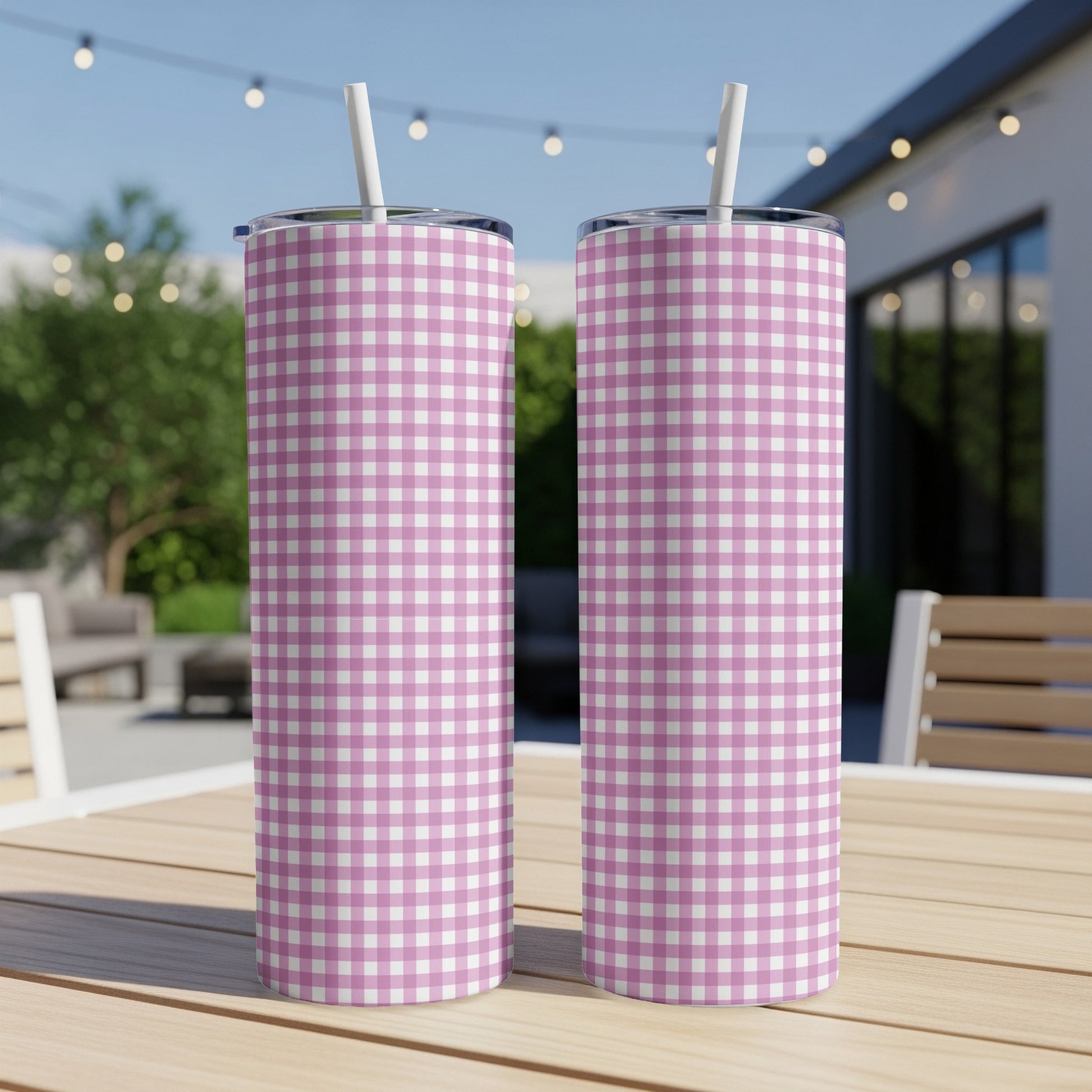 Two pink and white gingham pattern tumblers with straws on a wooden table.