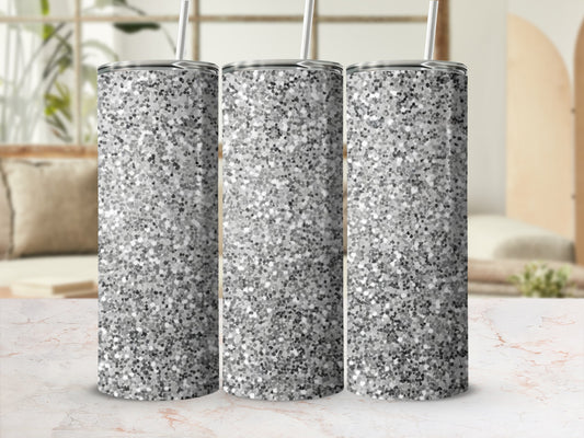 Three silver glitter tumblers with straws on a patterned surface.