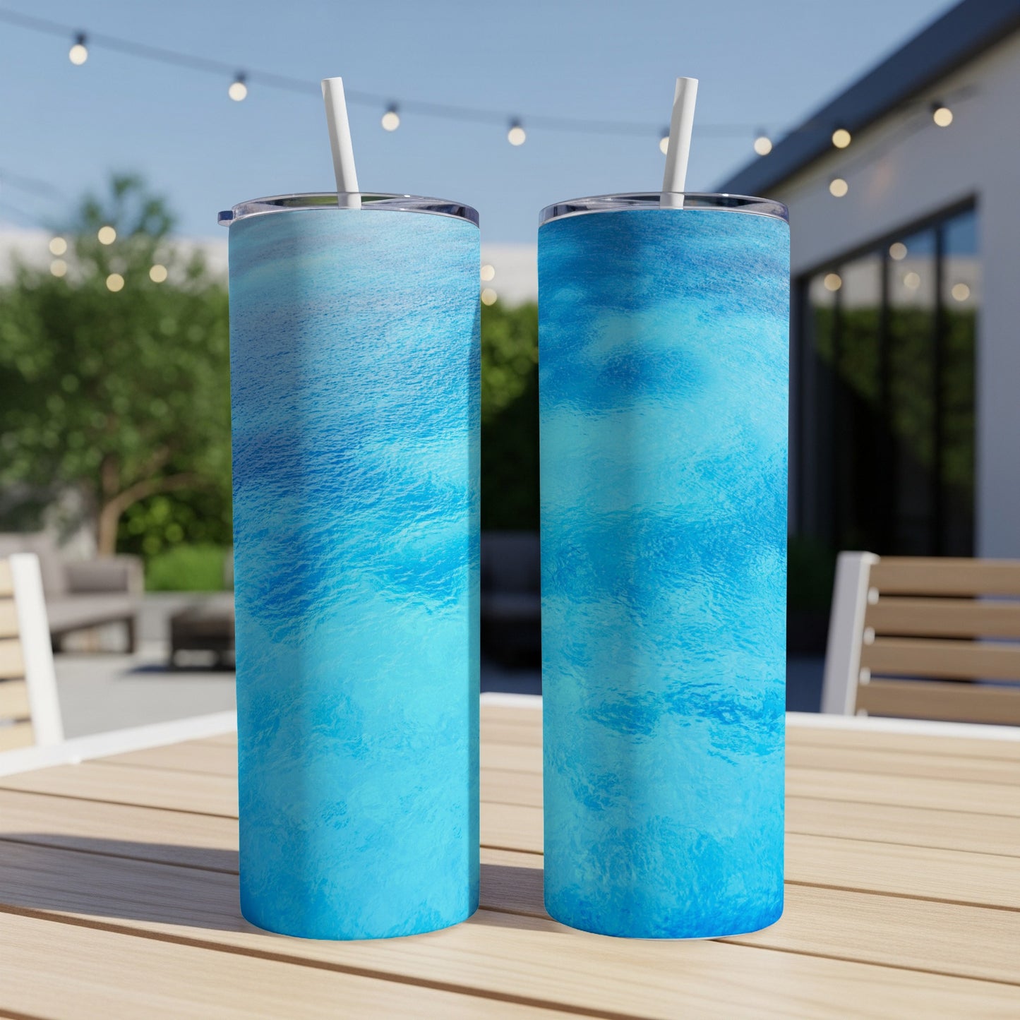 Two blue ocean wave pattern tumblers on a wooden table with outdoor background.