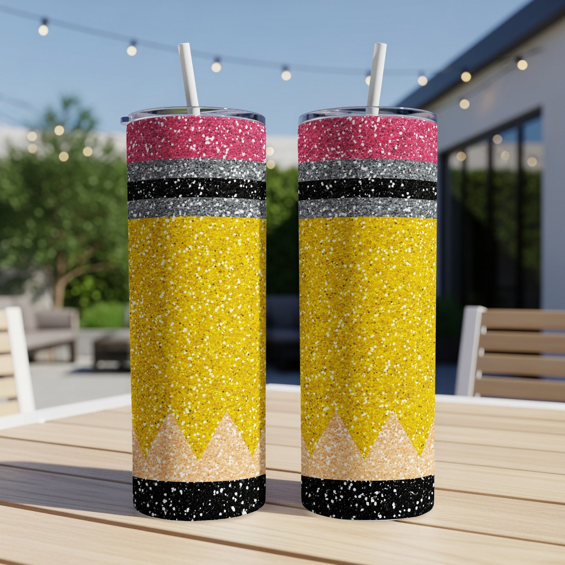 Two glittery yellow pencil tumblers with pink and black lids stand on a table.