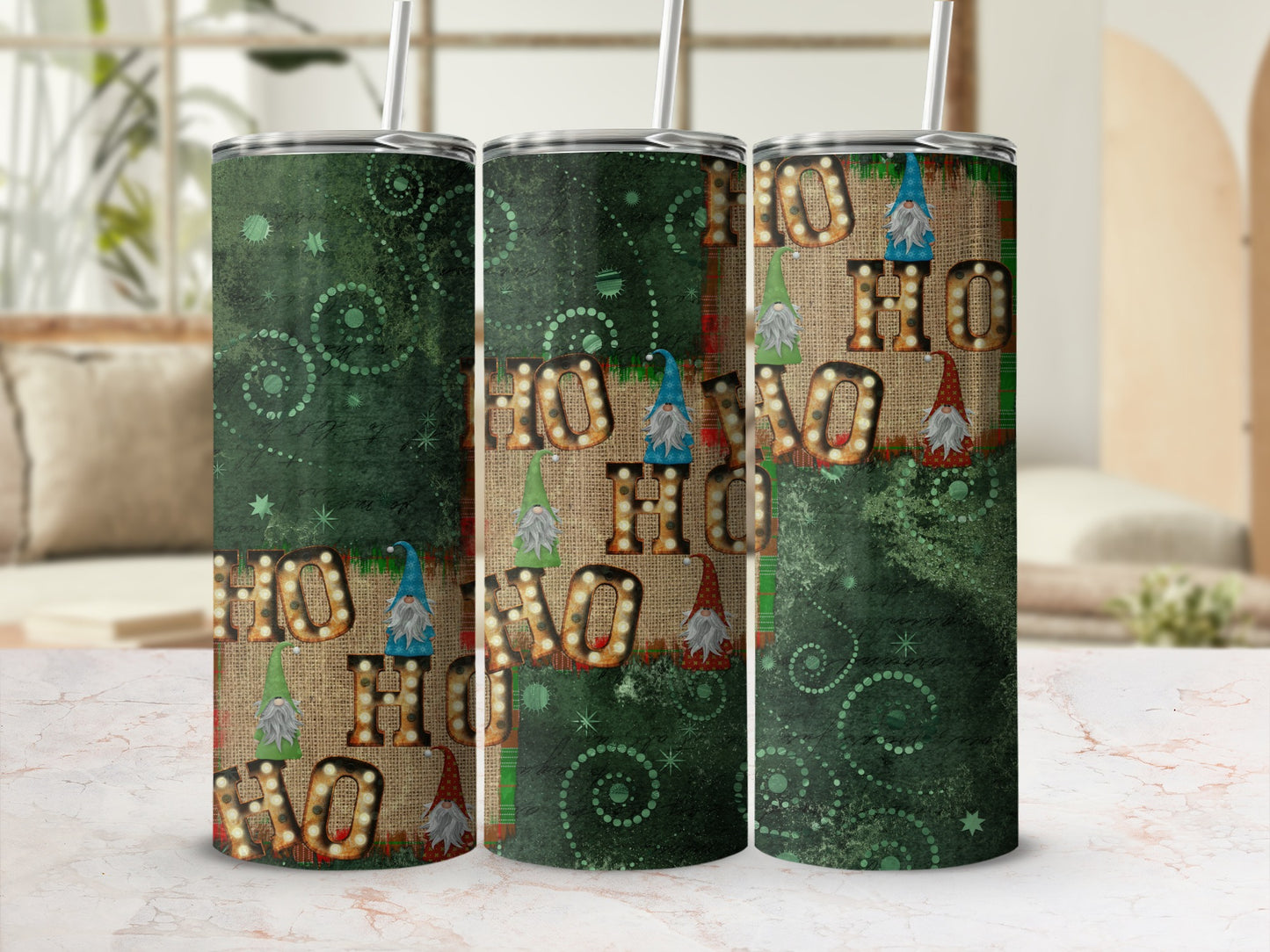 Three tumblers with "HO HO HO" and gnome designs on a marble surface.