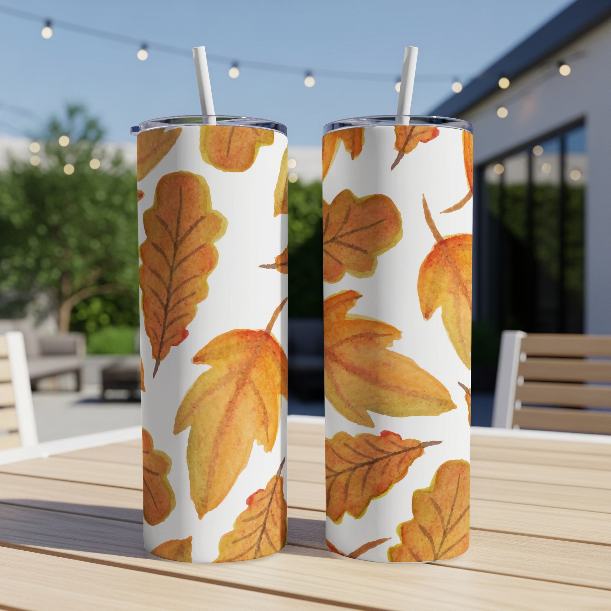 Two tumblers with an autumn leaf pattern on a table outdoors.