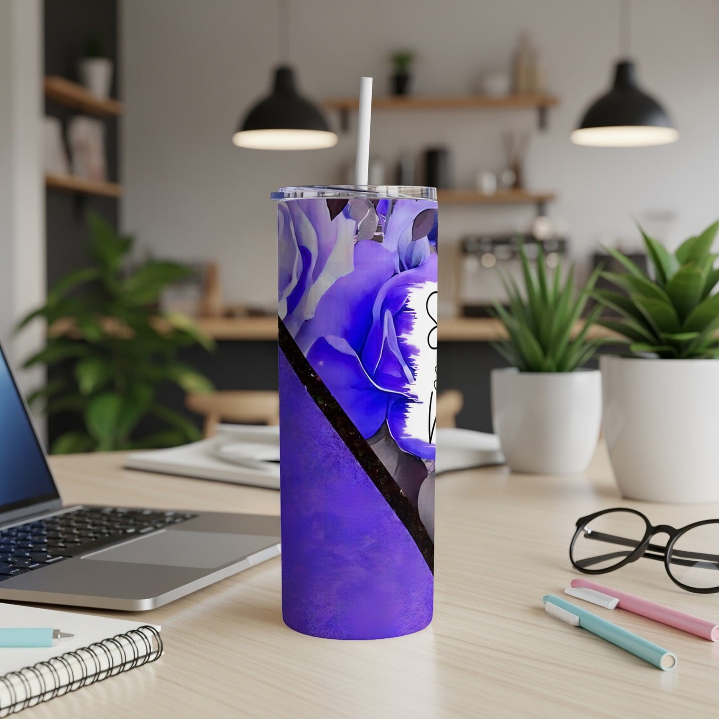 Purple floral tumbler with straw on desk with laptop and pens.