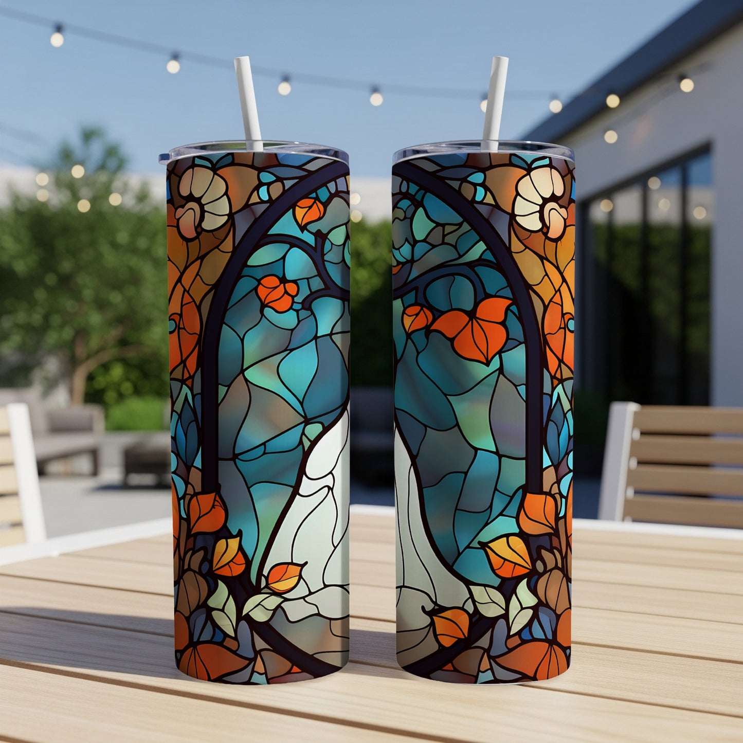 Two stained glass tumblers with autumn leaf patterns sit on a table outdoors.