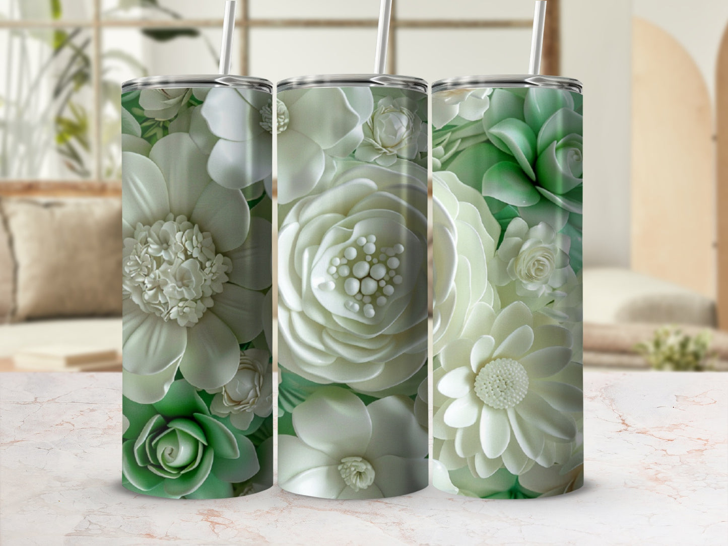 Three tall, white and green floral tumblers with straws on a marble surface.