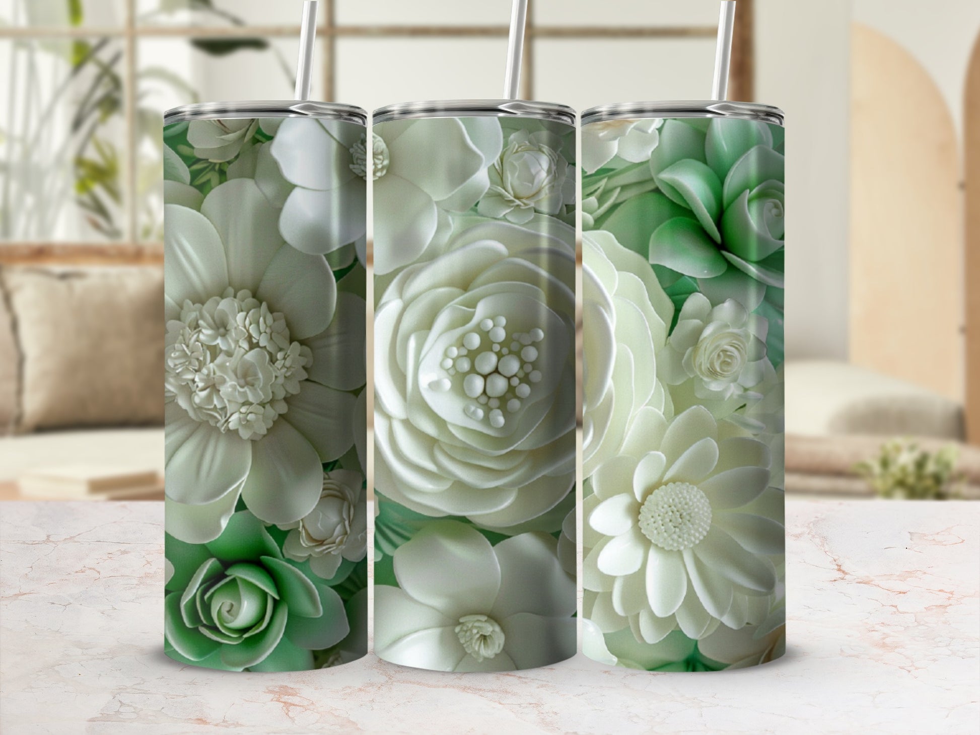Three tall, white and green floral tumblers with straws on a marble surface.