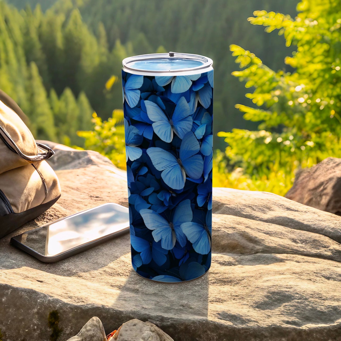 Blue butterfly pattern on a tumbler with phone and bag in background.