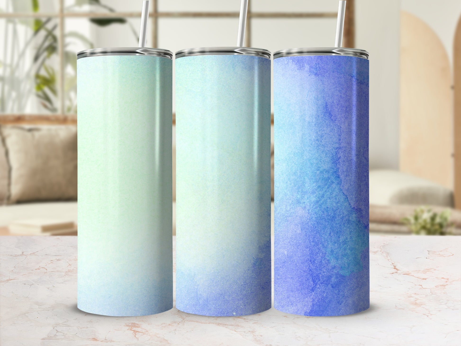 Three tumblers with ombre blue and green watercolor designs, standing on a marble surface.