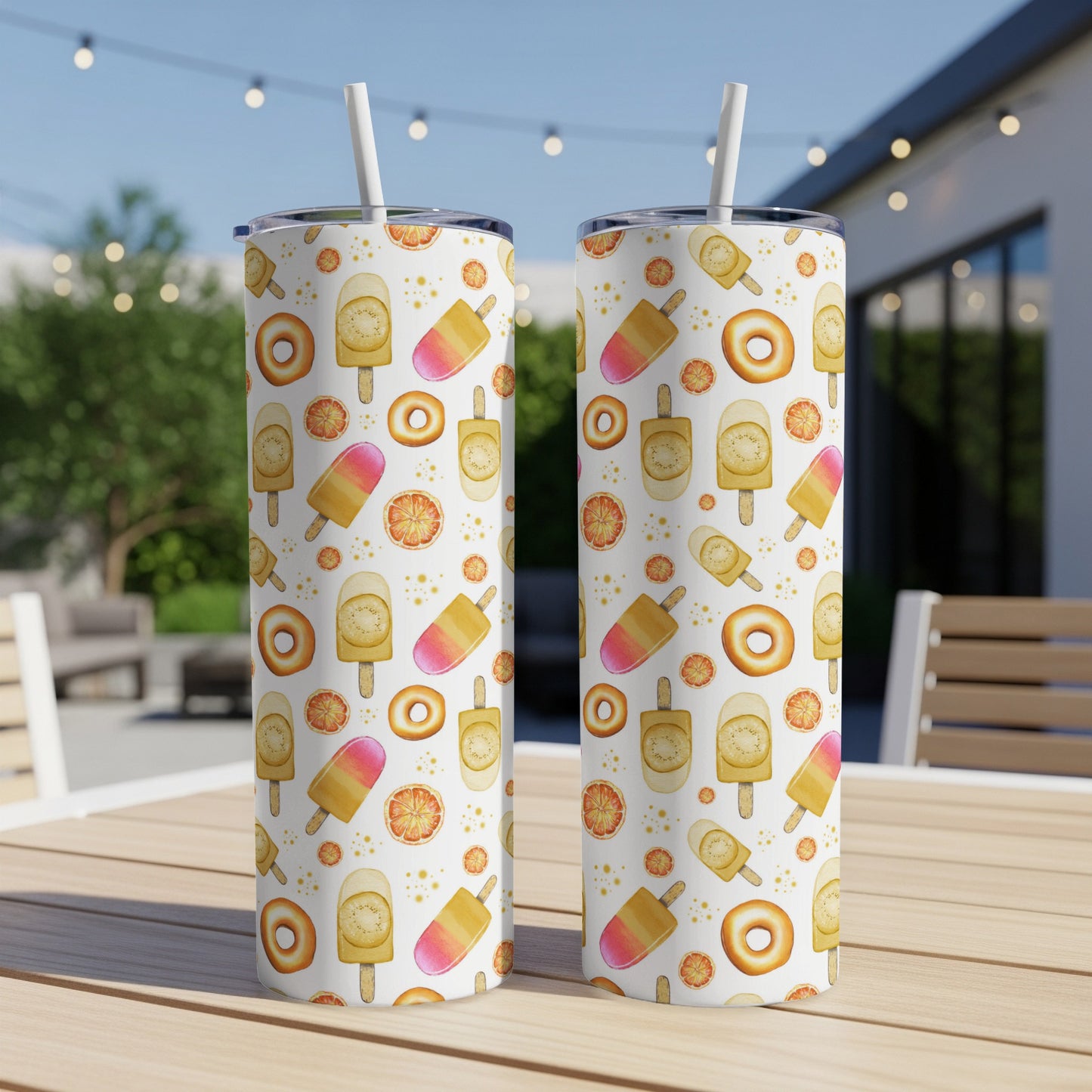 Two tumblers with a pattern of popsicles, donuts, and oranges on a patio table.