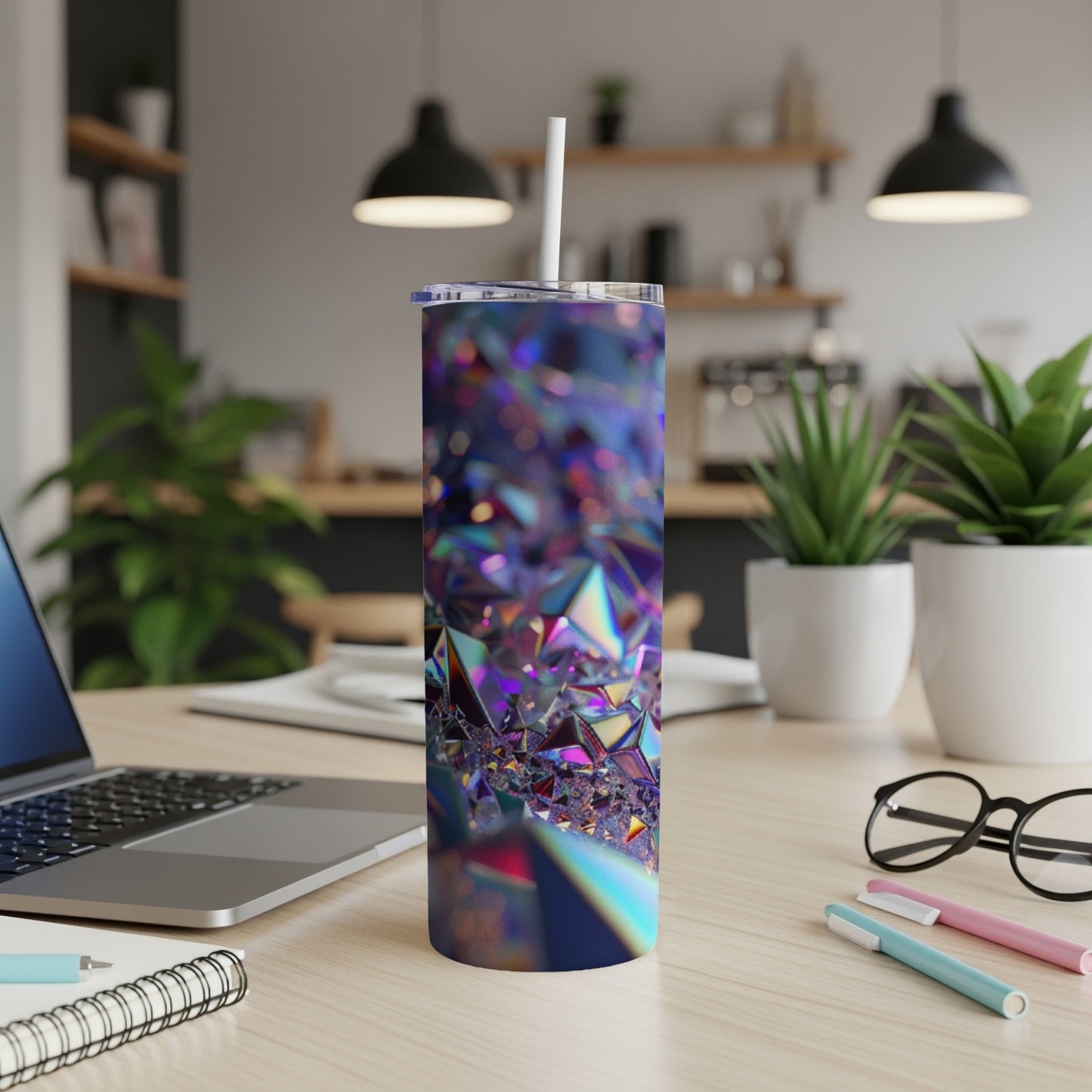 Iridescent faceted tumbler with straw on desk with laptop and pens.