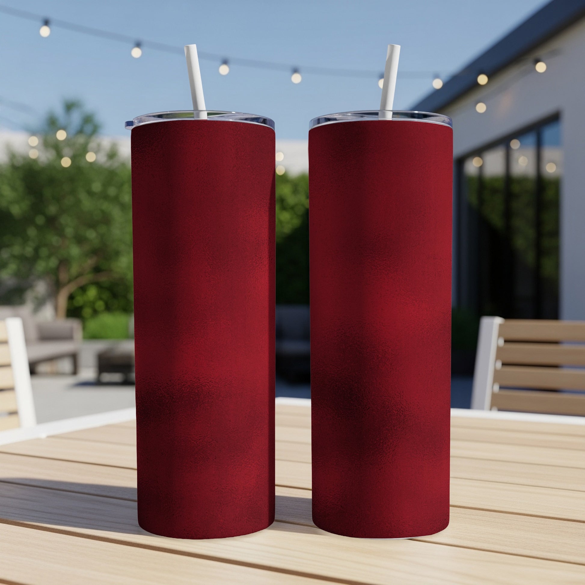 Two dark red speckled tumblers with white straws sit on a wooden table outdoors.