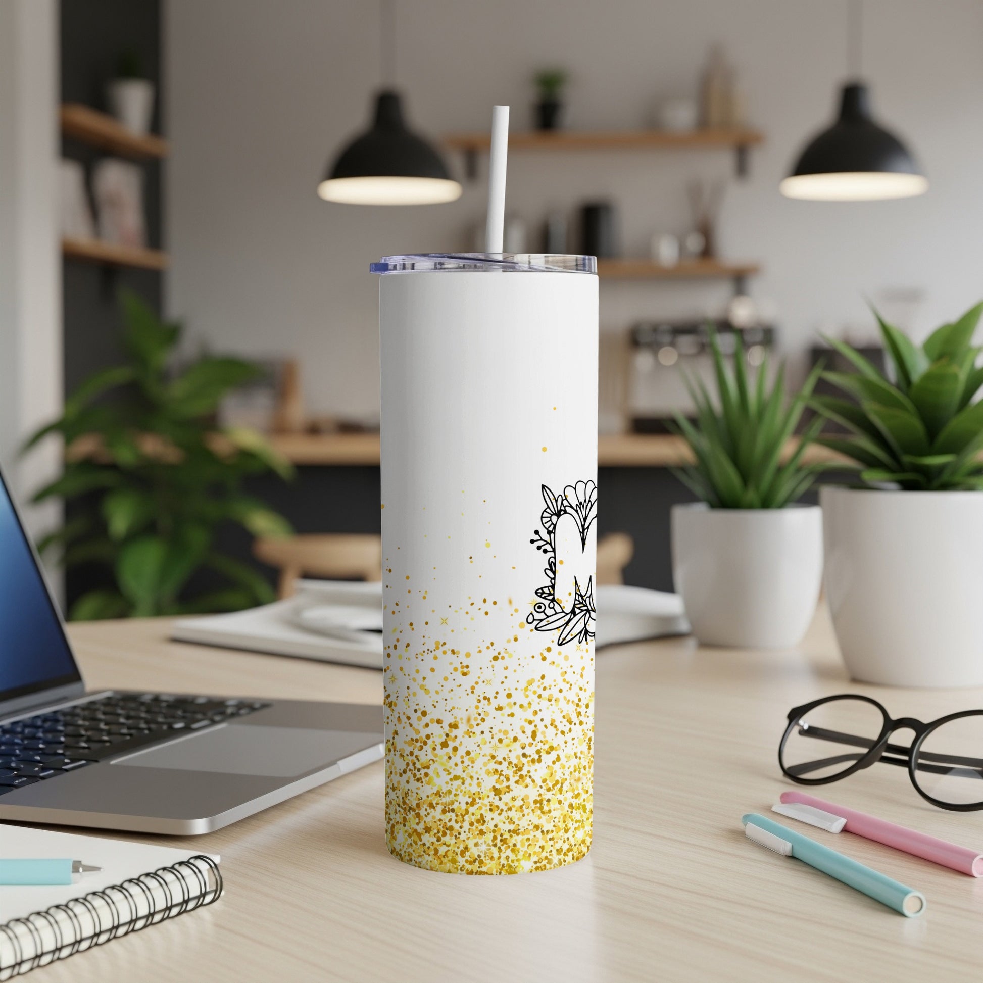White tumbler with gold glitter accents and floral "M" design.