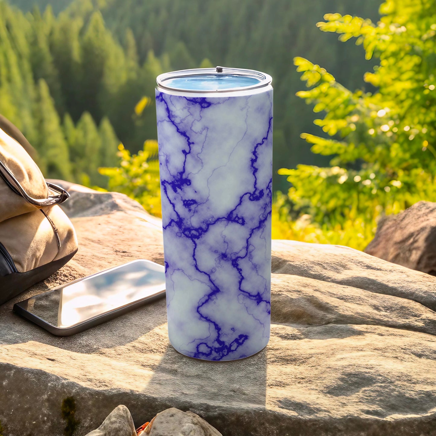 Blue marble patterned tumbler with phone and bag on rocks.