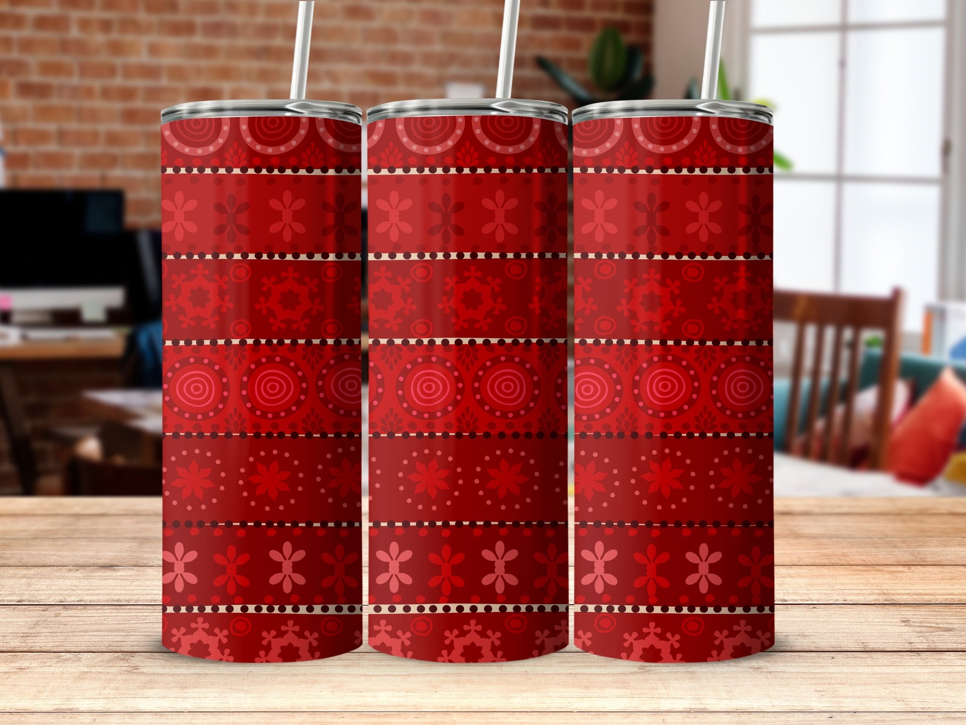 Three red tumblers with festive patterns on a wooden table.