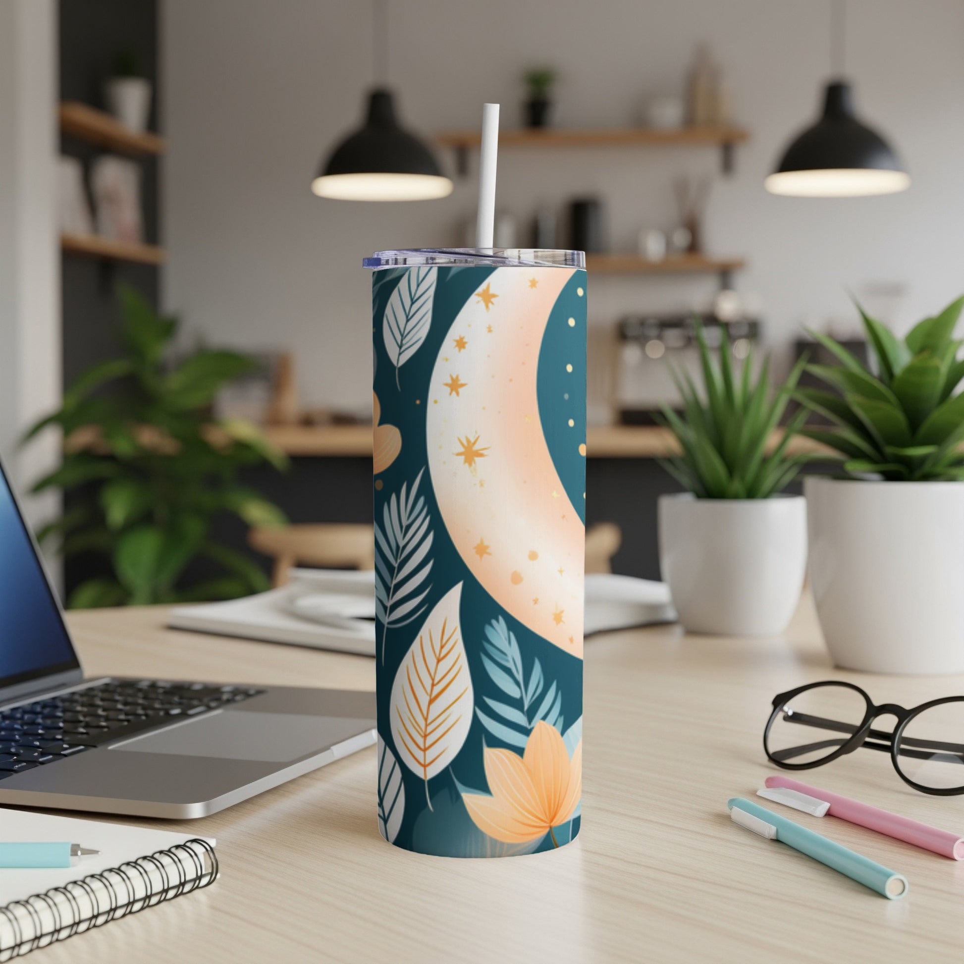 Tall tumbler with crescent moon, leaves, and stars design, on a desk.