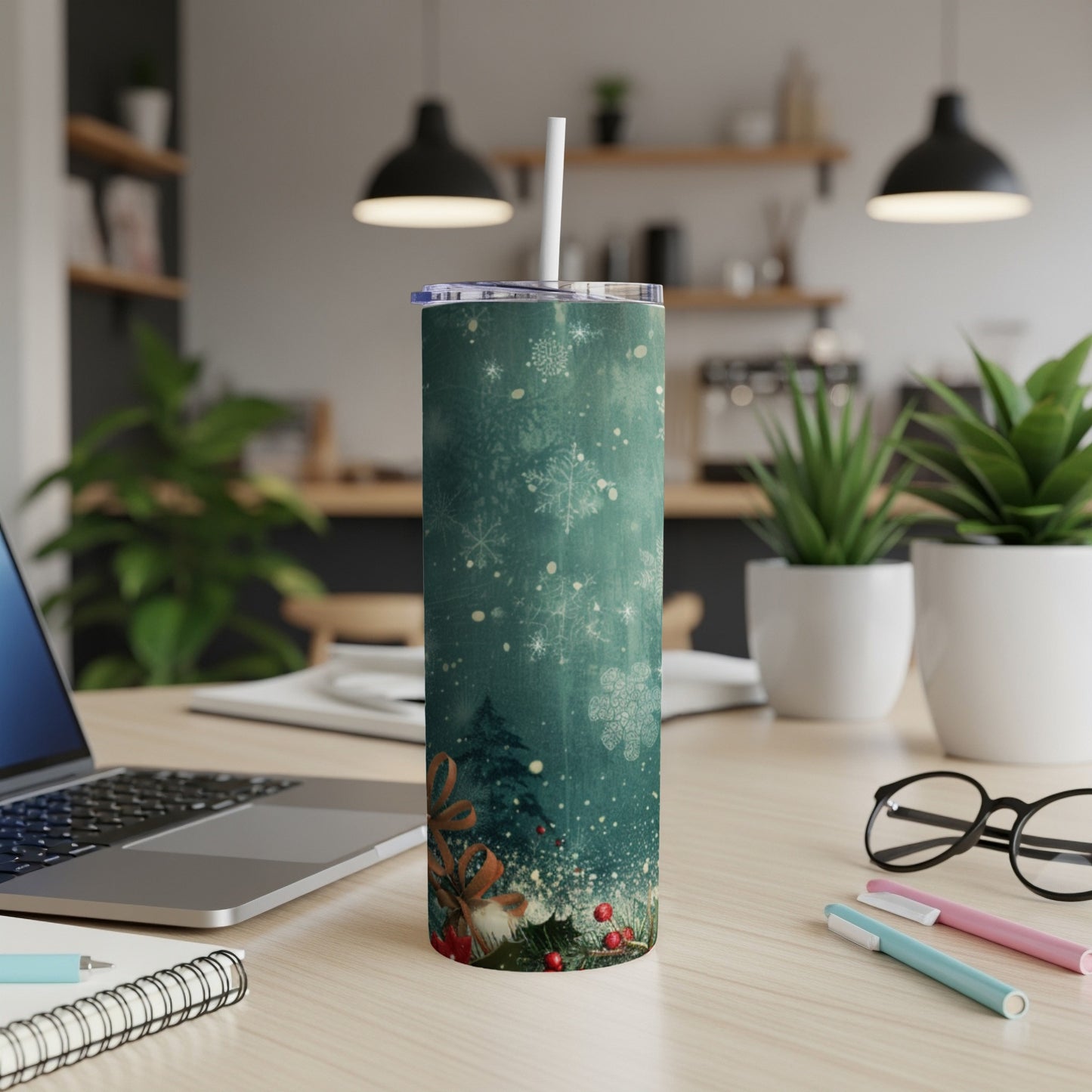 Teal tumbler with snowflakes and Christmas tree design on a desk.