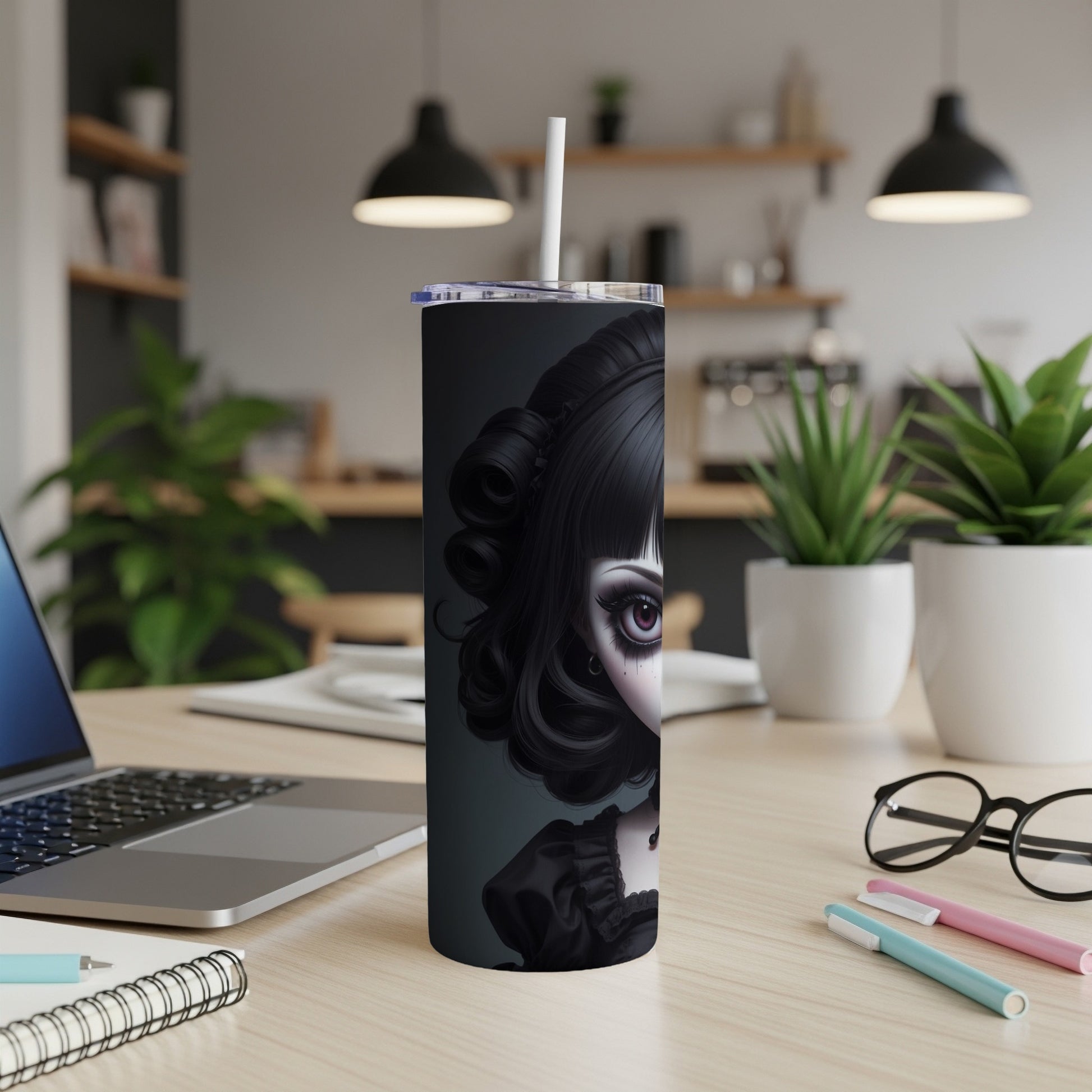 Gothic doll illustration on a black tumbler with straw on a desk.